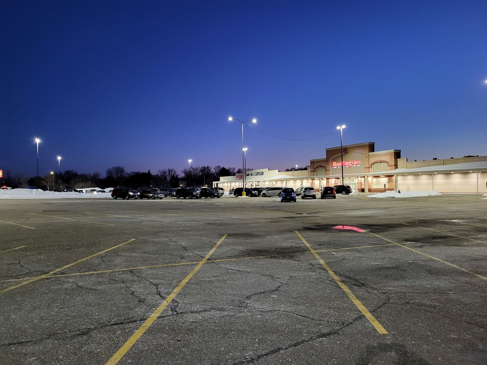 A dark, empty parking lot in front of a supermarket at dusk.