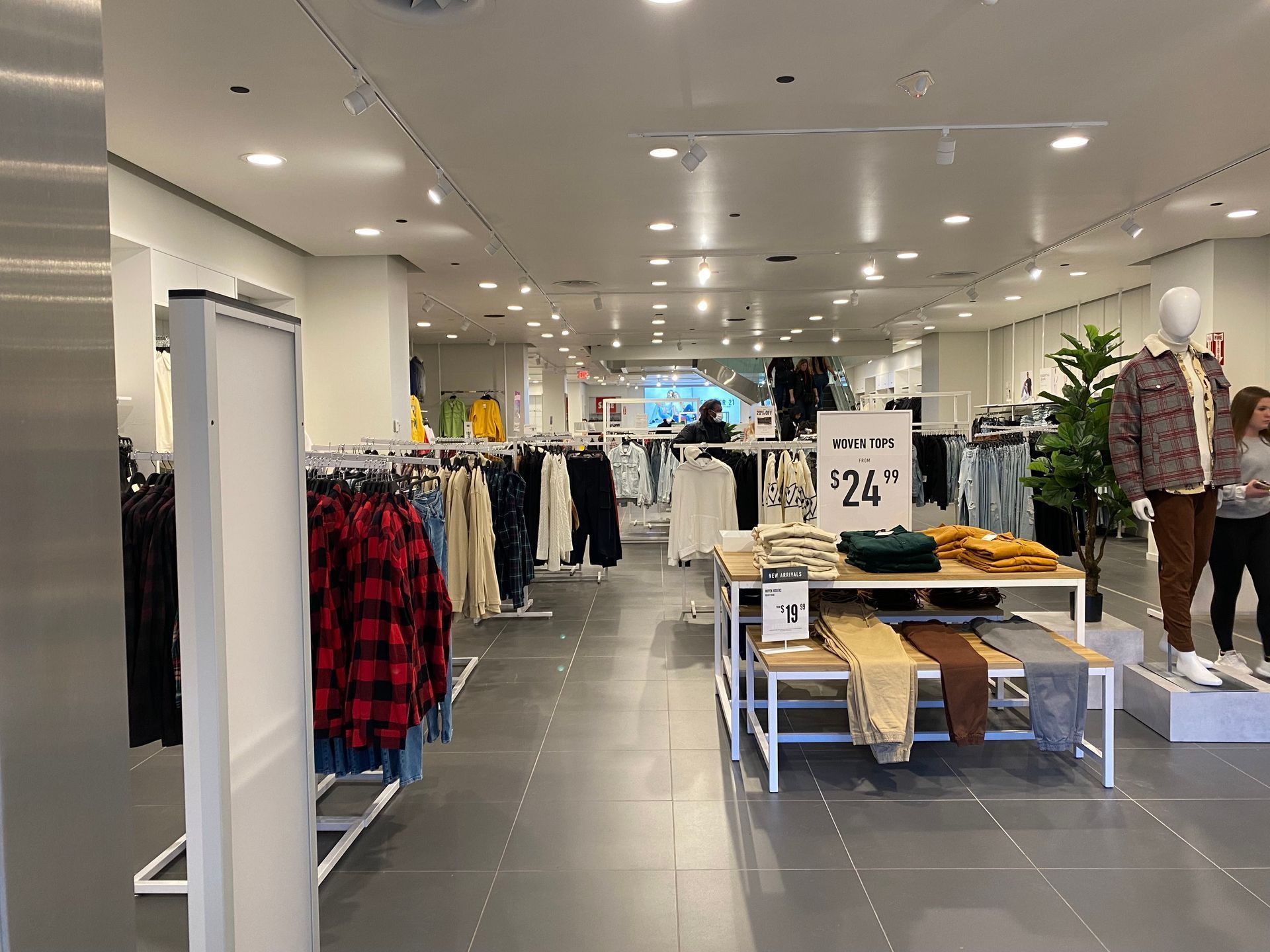 Clothing store interior with racks of apparel and mannequins. White walls, gray floor, and bright lighting.