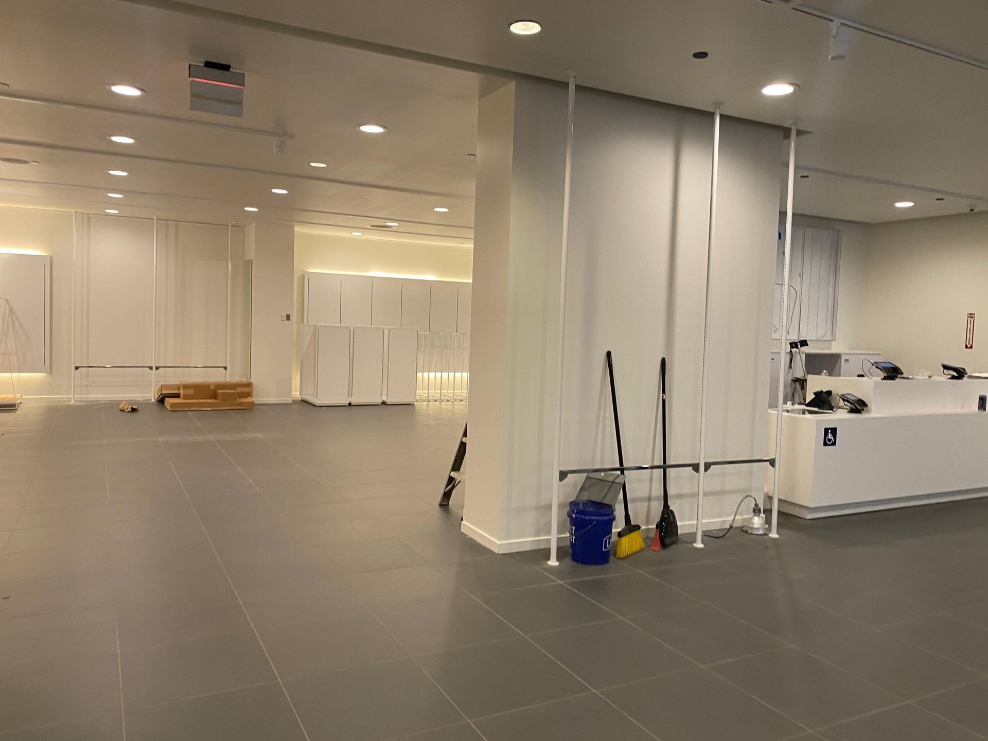 Empty retail space, white walls, gray floor, construction materials, cleaning supplies.
