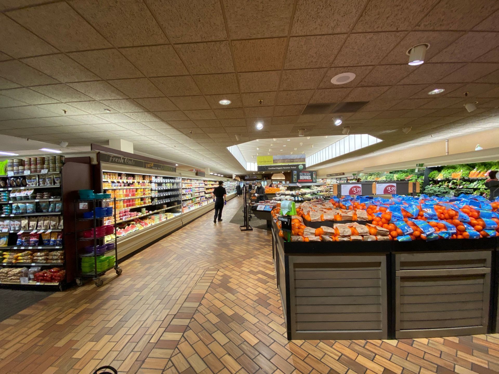 Grocery store interior with produce display, aisles of food, and customers shopping.