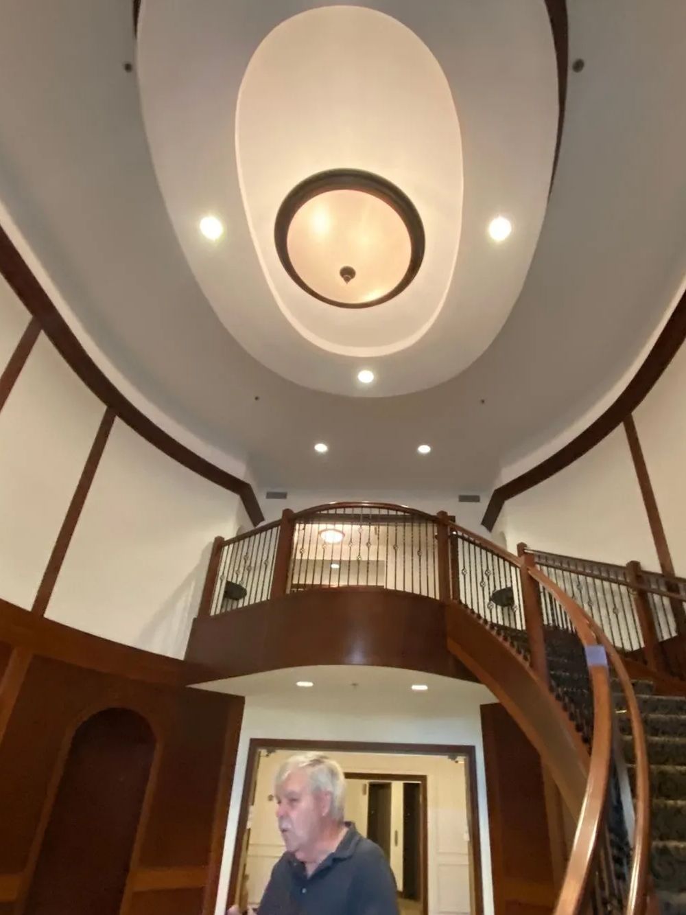 Man standing in an entryway with a spiral staircase, balcony, and ceiling light fixture.