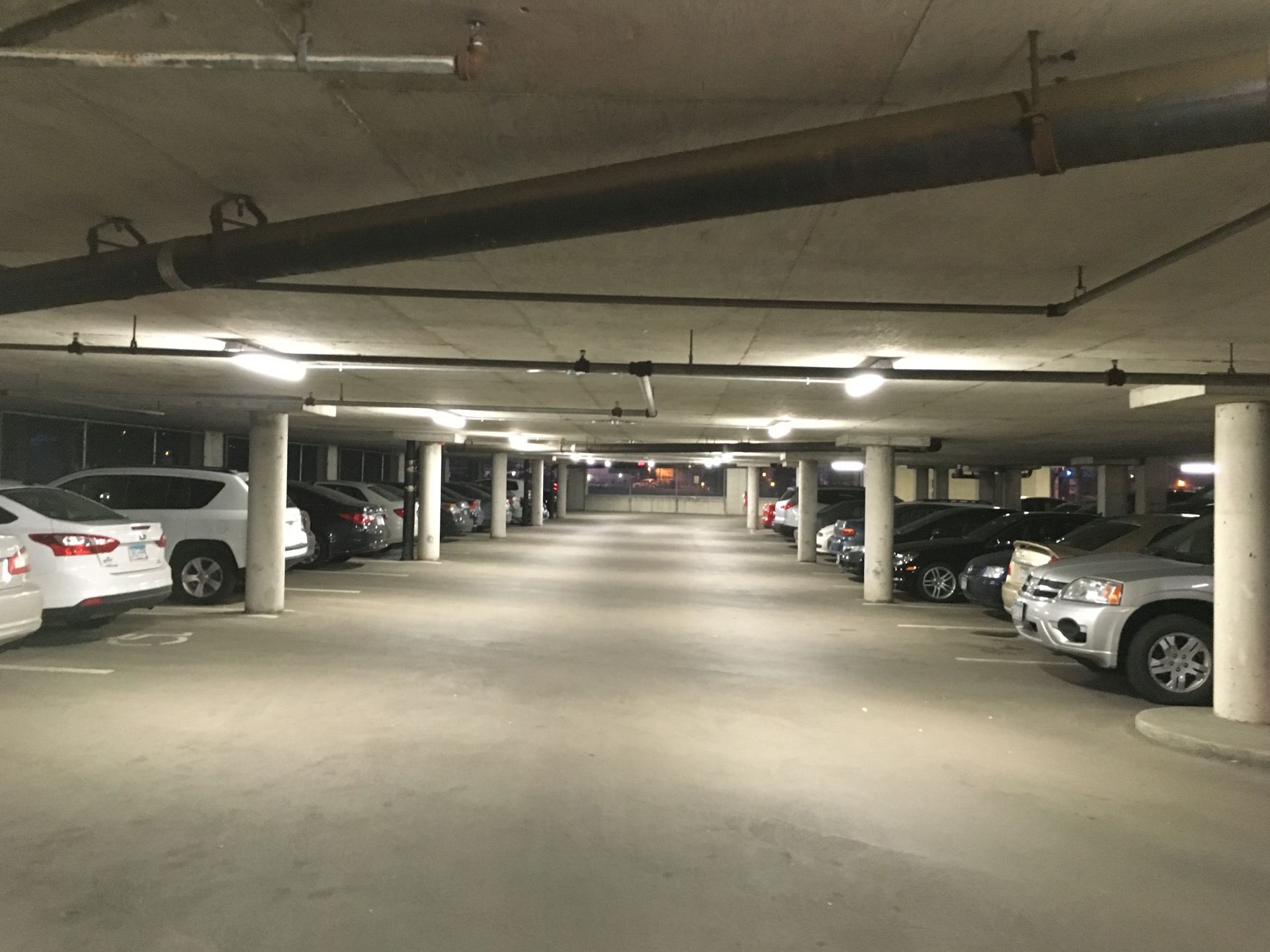 Underground parking garage with cars parked in rows, illuminated by overhead lights.