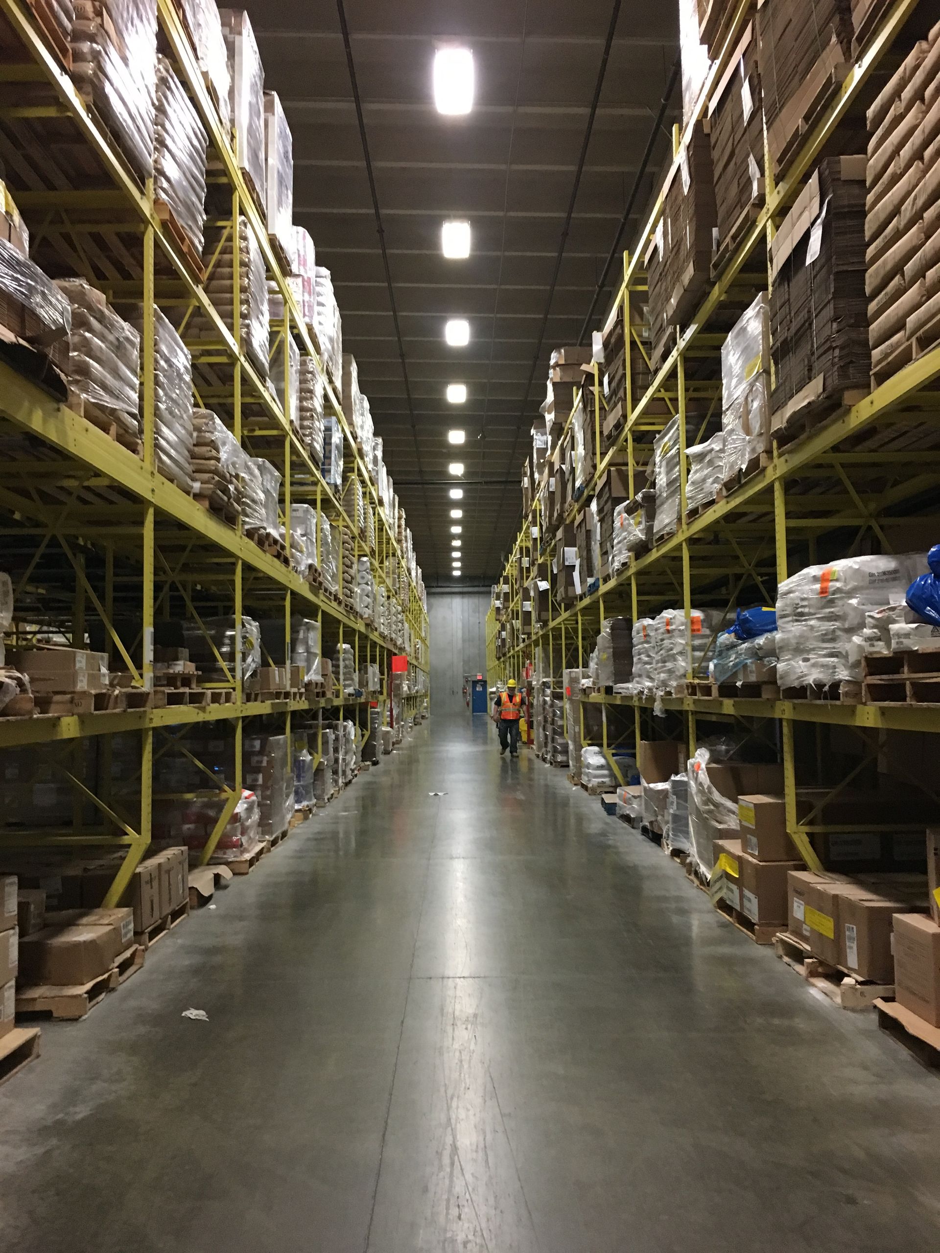 Warehouse aisle with tall yellow shelves stacked with packaged goods.