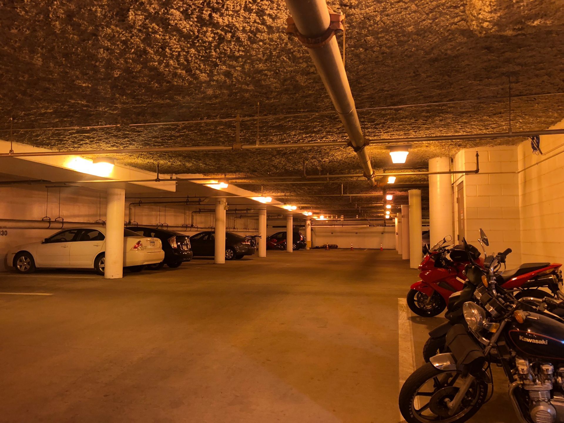 Indoor parking garage with cars and motorcycles parked. Brightly lit with overhead lights.
