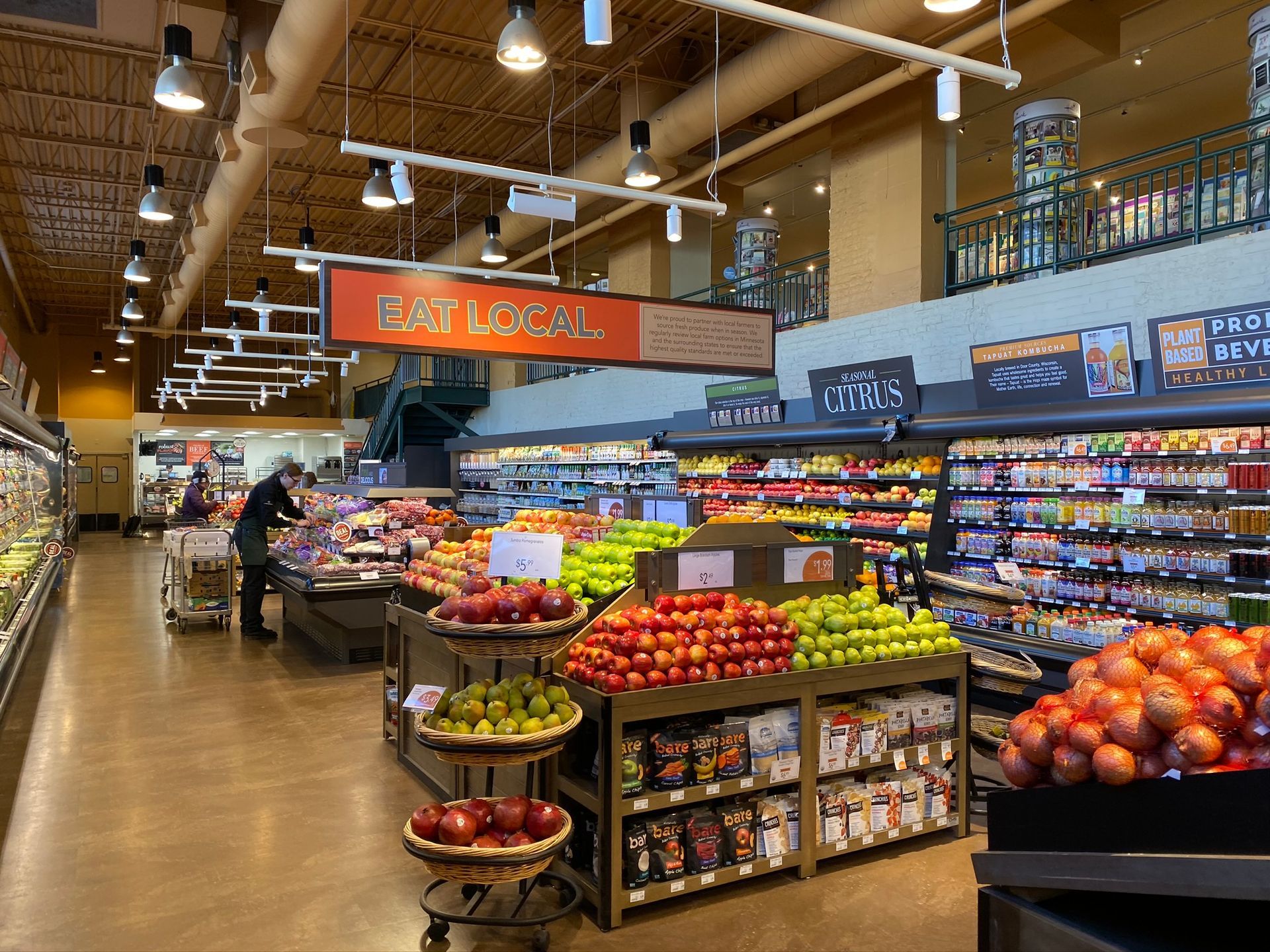 Interior of a grocery store with produce section, well-lit; person shopping, shelving stocked with fruits, vegetables, and packaged goods.