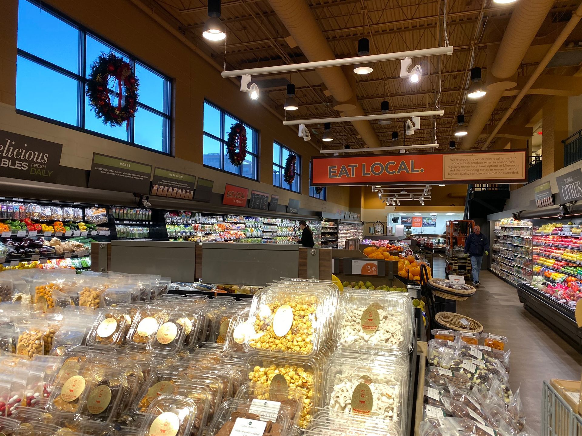 Grocery store aisle with packaged snacks, refrigerated food cases, and overhead lighting.