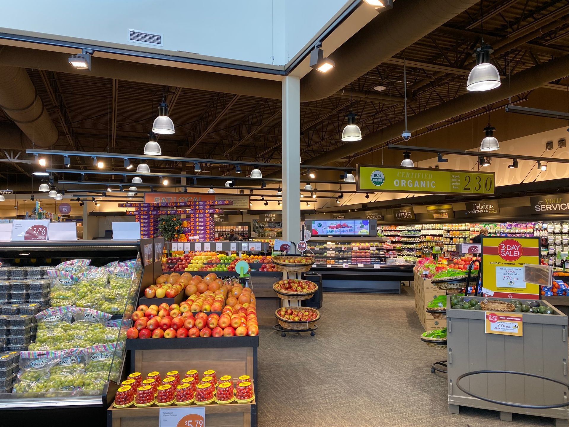 Grocery store produce aisle, featuring fruit displays and overhead lighting.