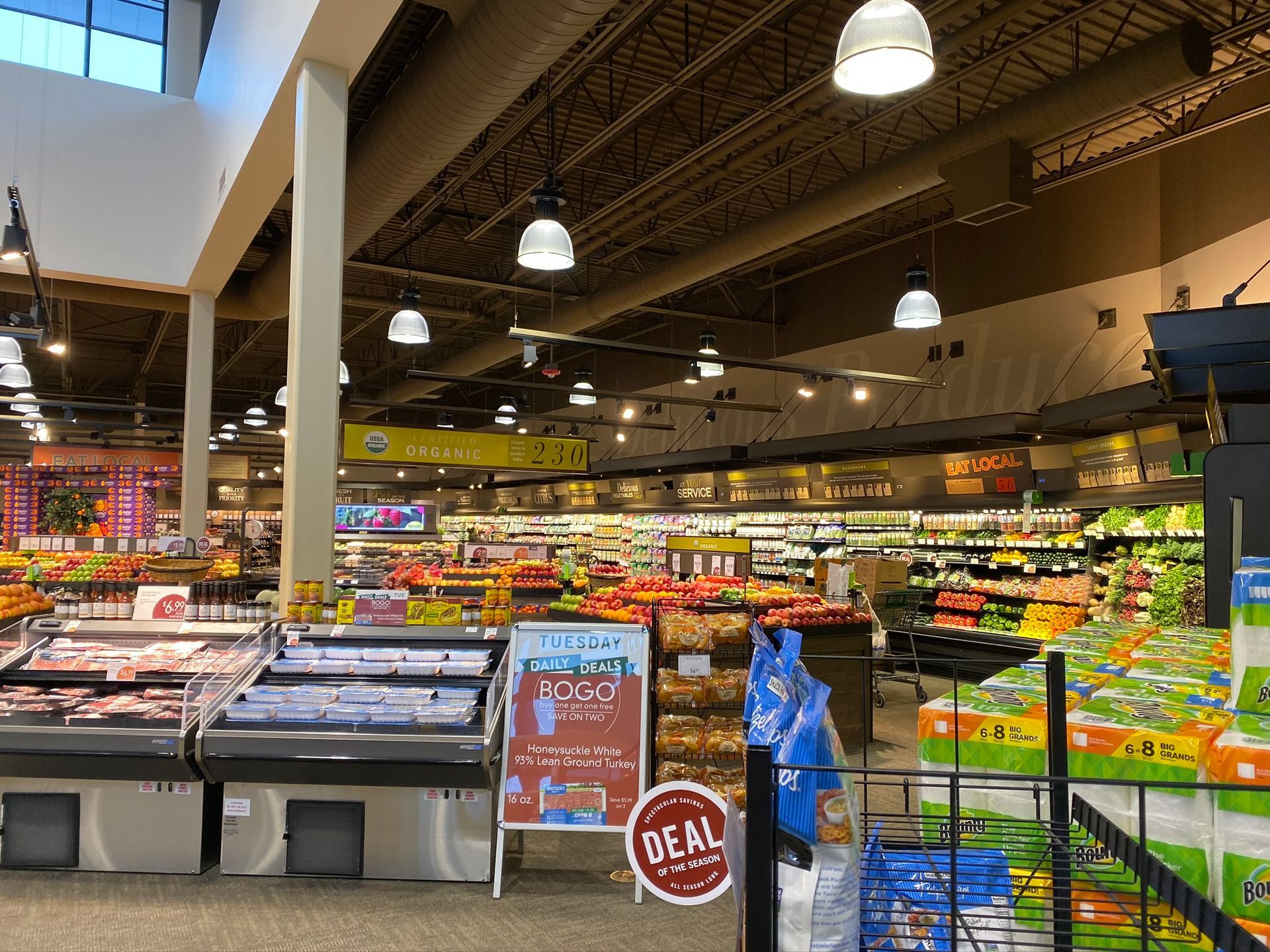 Grocery store interior with produce and meat displays under bright lights.