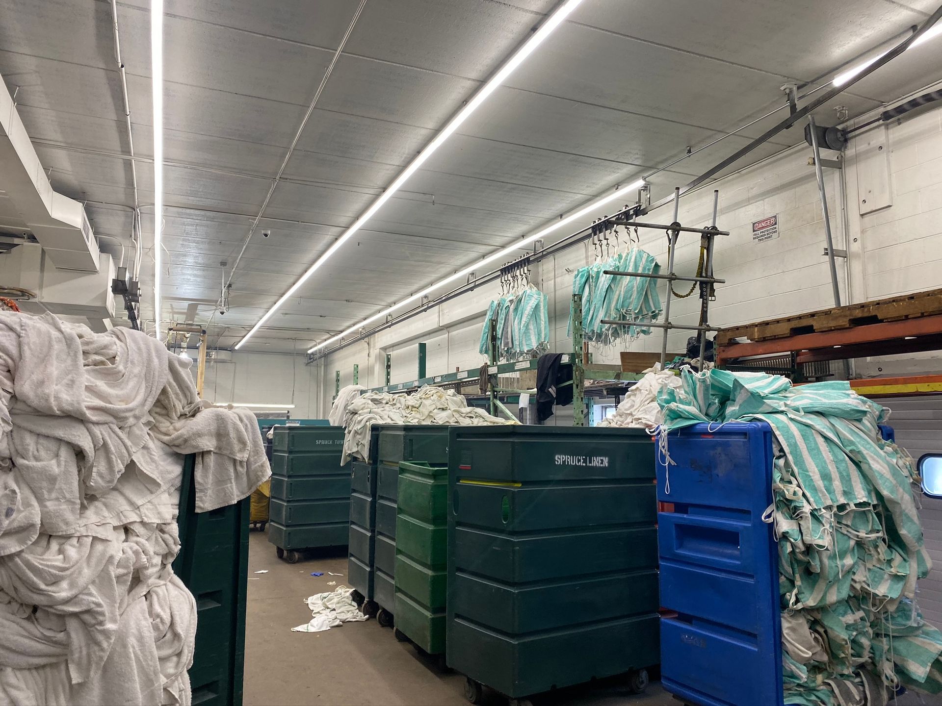 Laundry room with stacks of linens, green and blue bins, and overhead lighting.