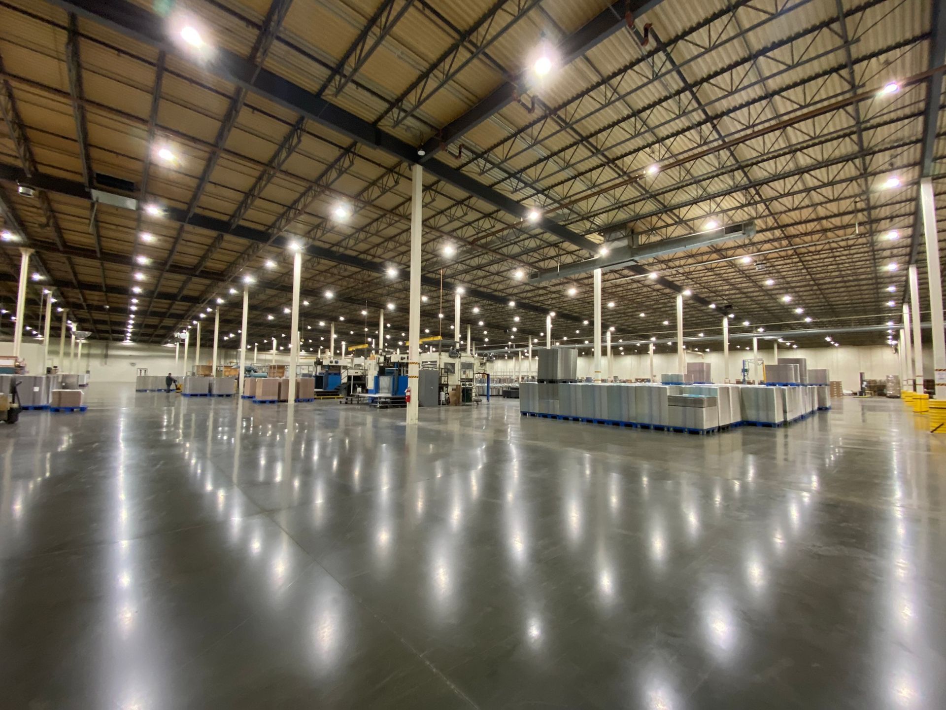 A wide-angle view of a vast, clean, industrial warehouse with shiny floors, tall support columns, and overhead lighting.