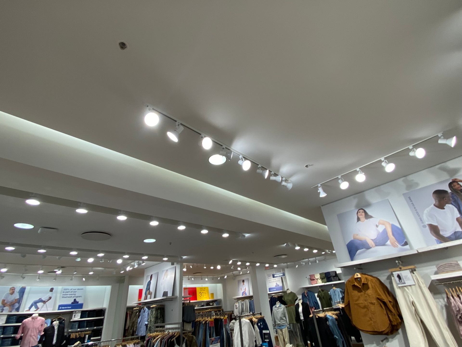 Interior view of a clothing store with bright overhead lights and clothing displays.
