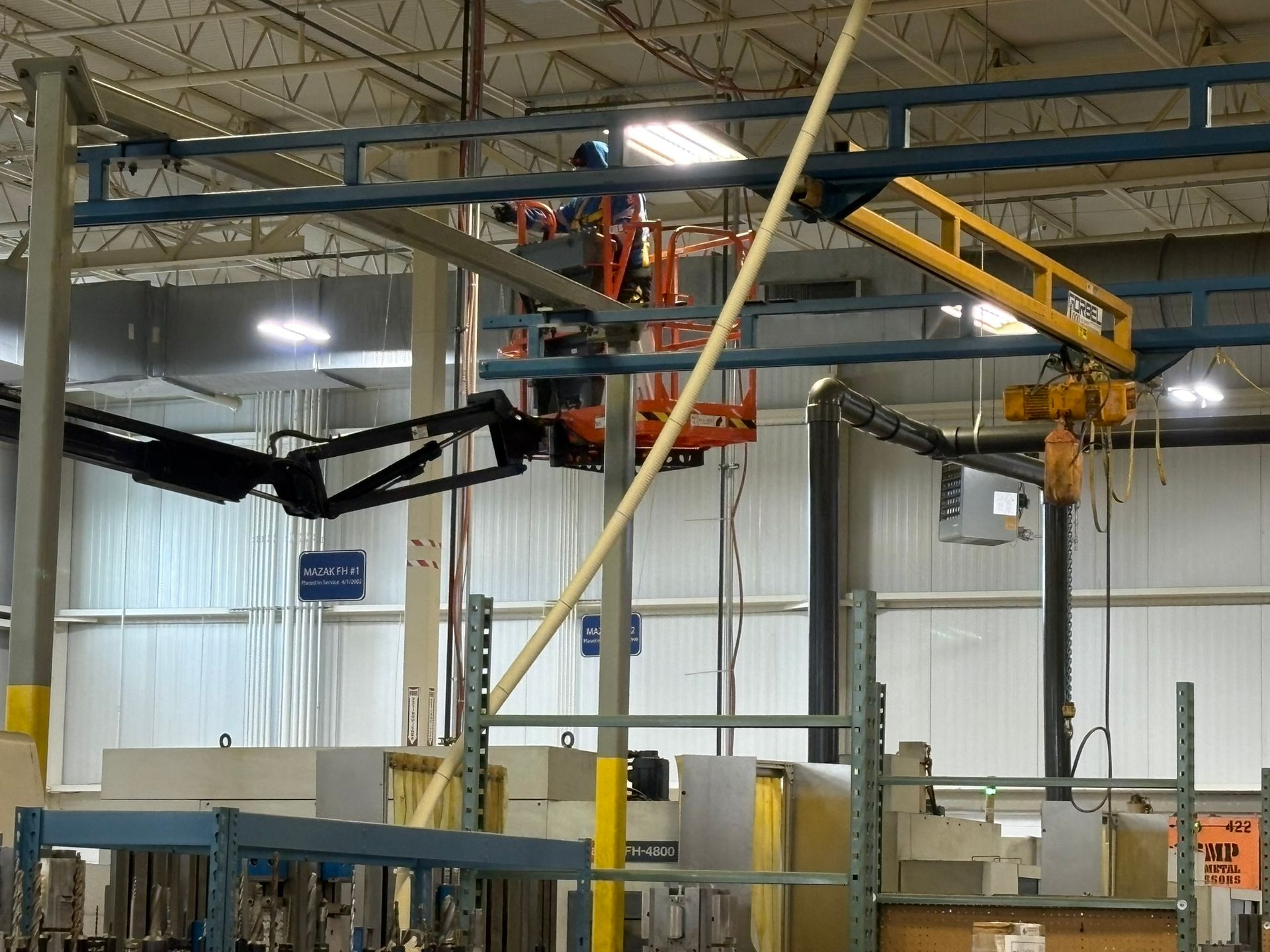 Worker in an orange lift operating near factory crane and overhead rails. Interior shot.