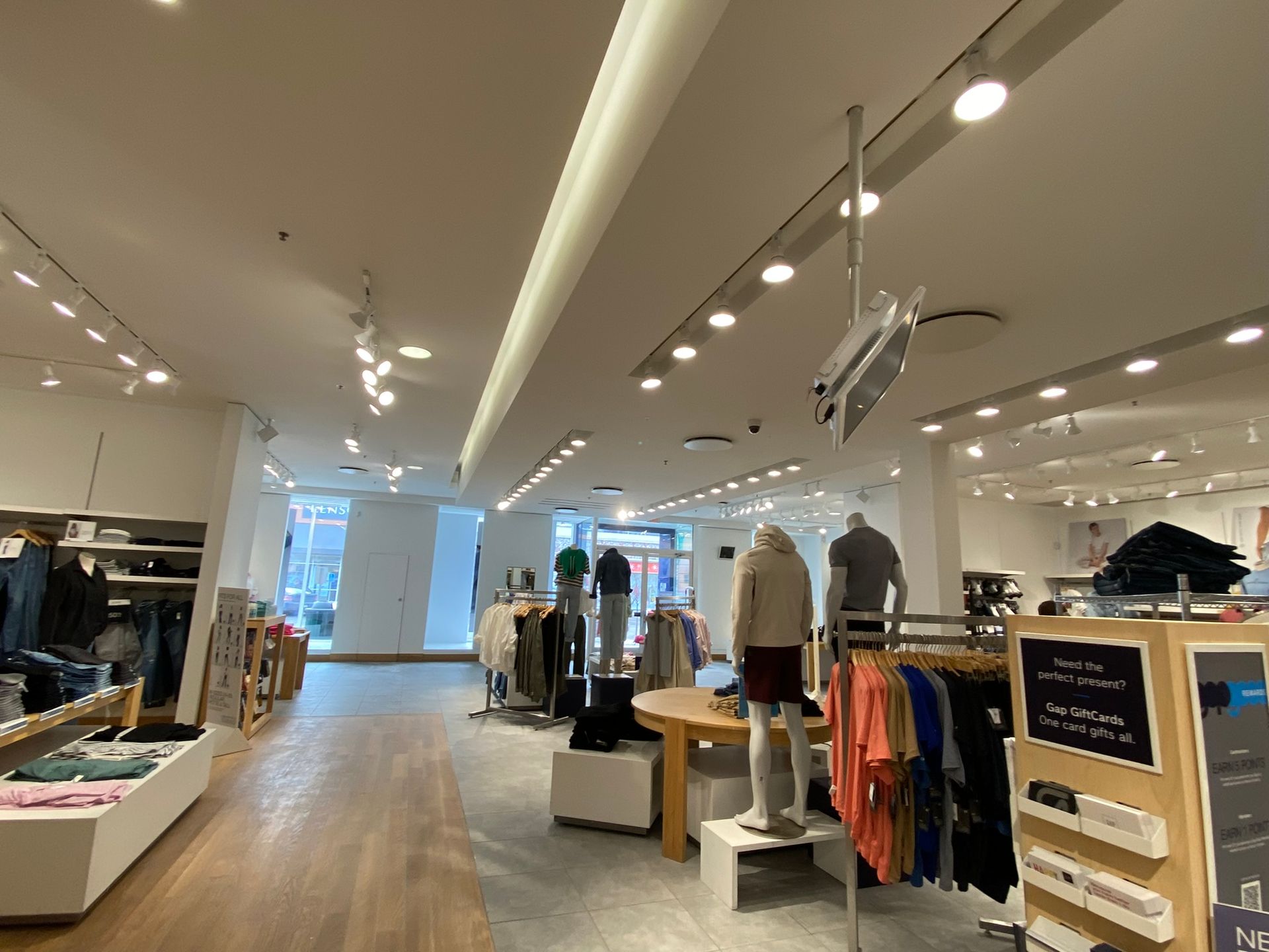 Inside a clothing store, mannequins and racks of clothes are displayed under bright lights.