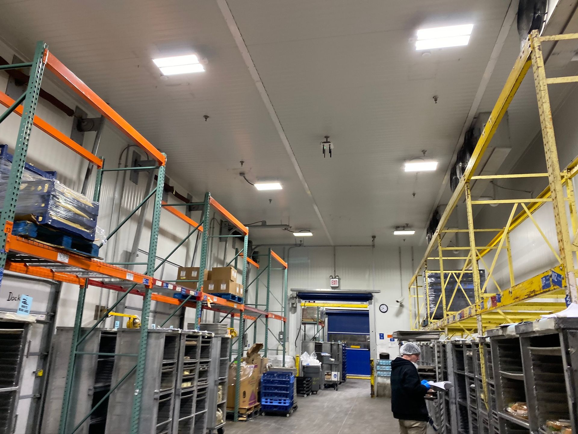 Warehouse with metal shelves holding boxes, food prep area, workers.