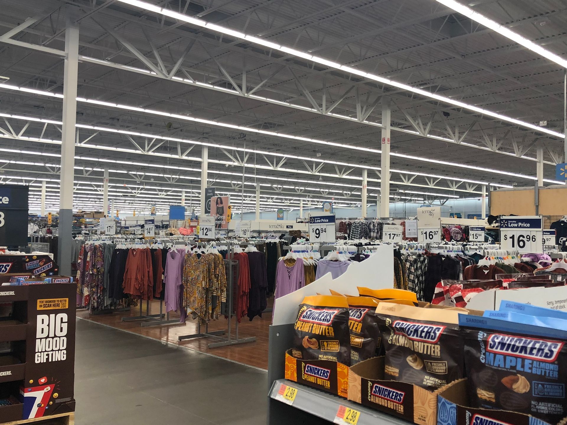 Interior of a Walmart store with clothing racks and snack displays under bright fluorescent lights.
