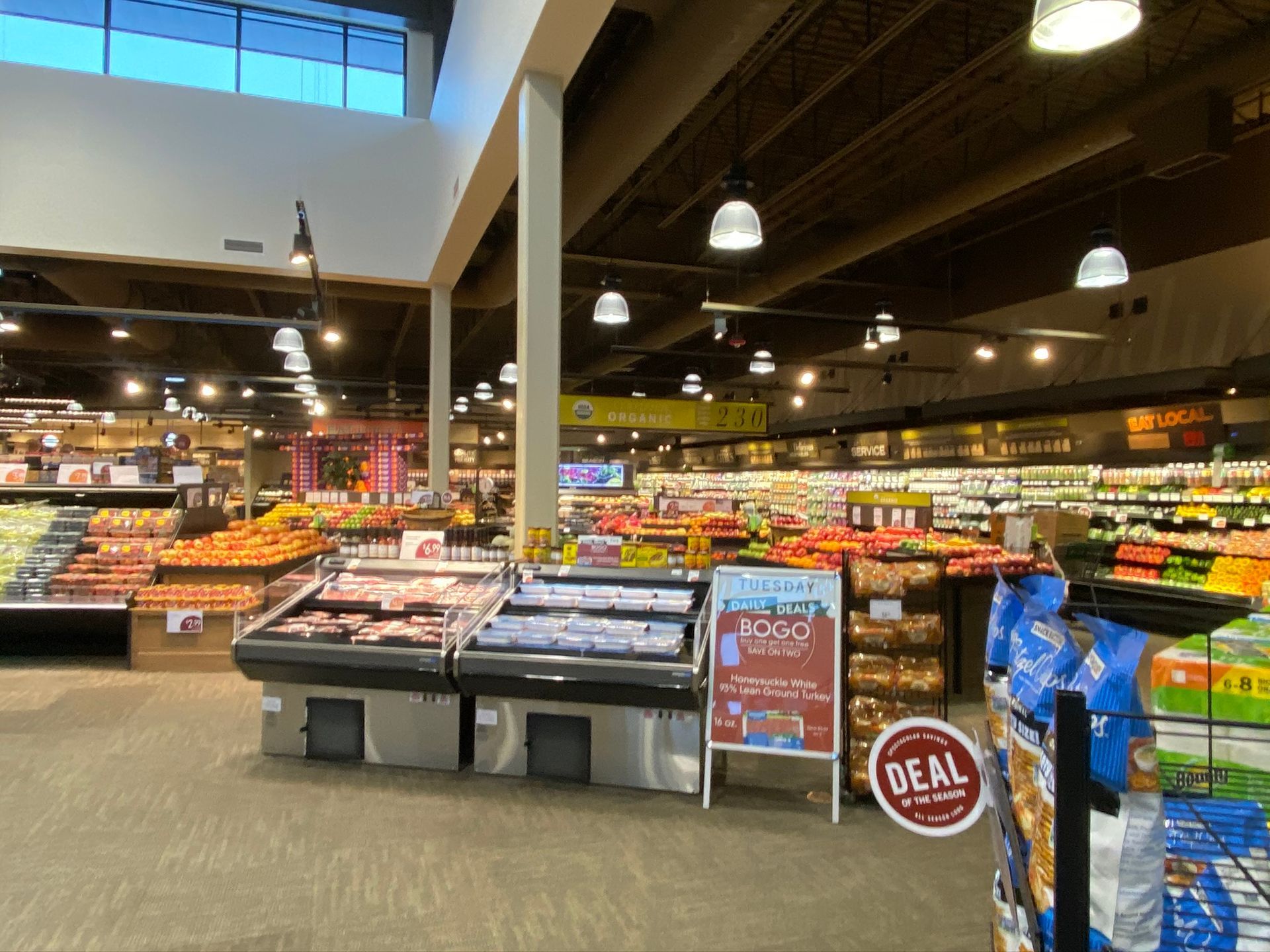 Grocery store interior with produce, meat counters, and aisle signs.