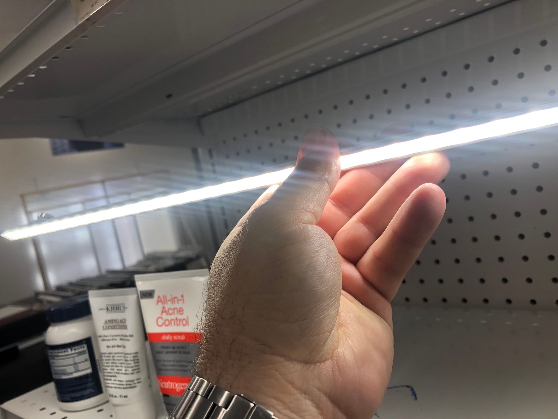 Hand reaching for a bright LED light strip on a store shelf, near skincare products.