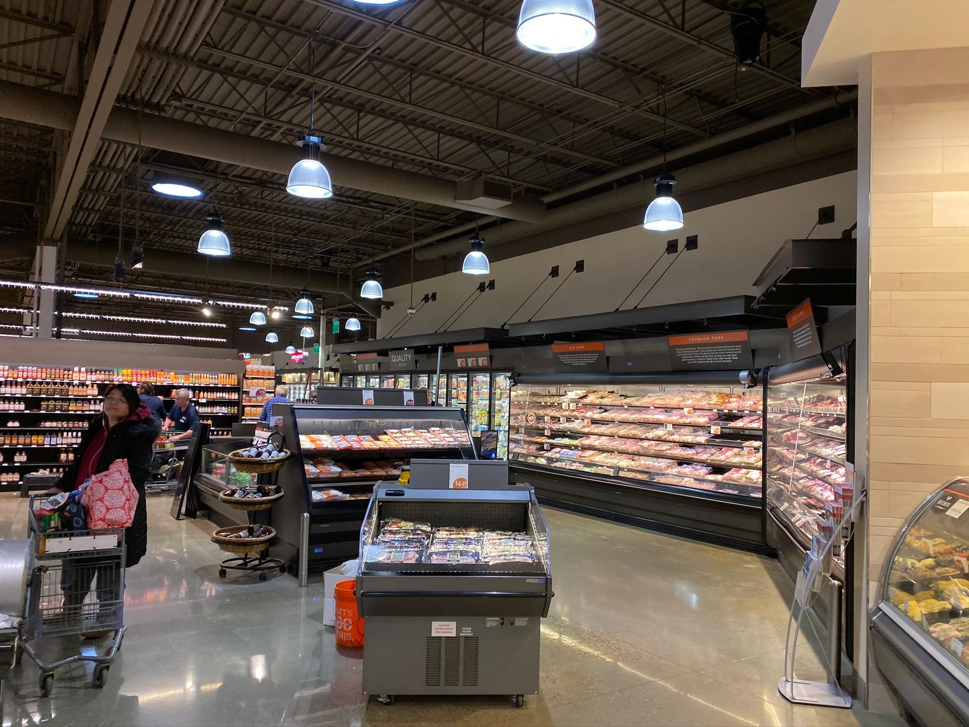 Interior of a supermarket with display cases of food, overhead lights, and a customer pushing a shopping cart.