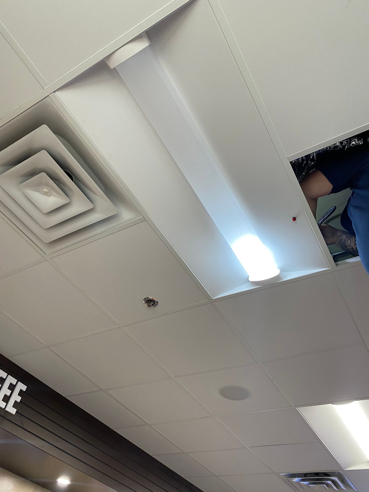 Ceiling with recessed lights, vents, and a person working on an open panel.