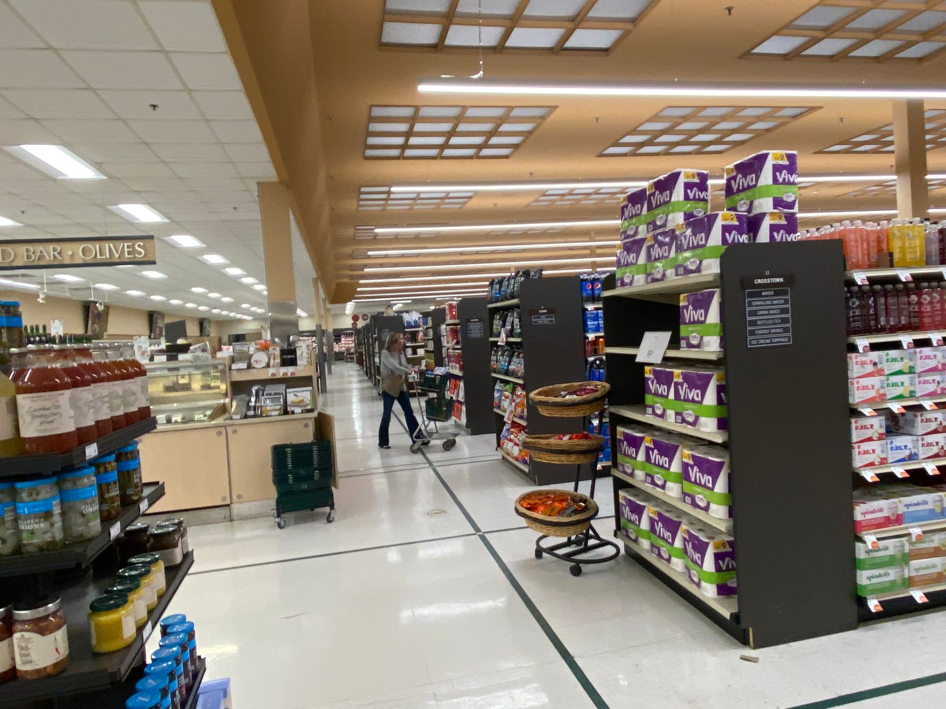 Grocery store aisle with shelves of products and a person pushing a shopping cart.