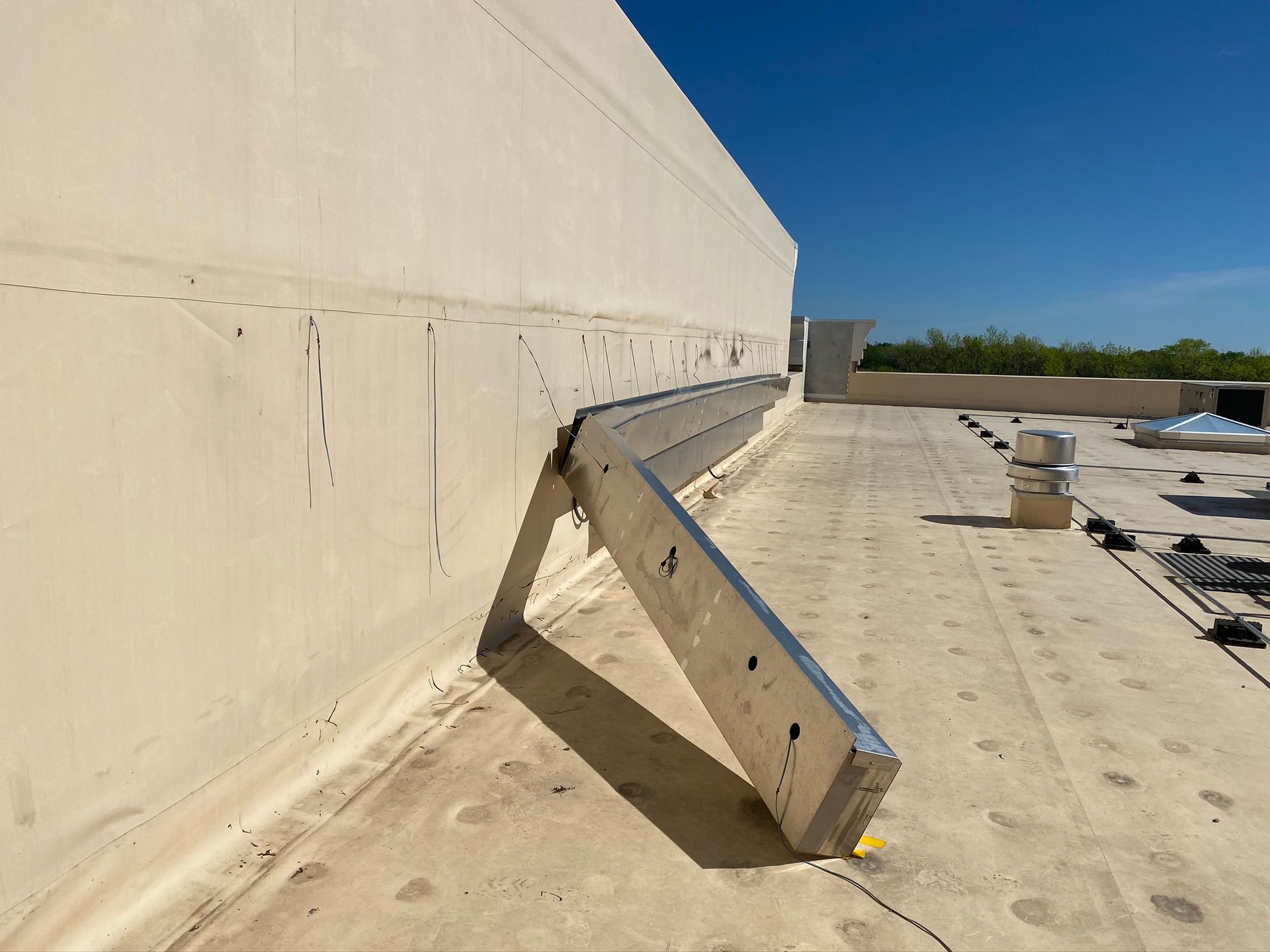 Metal ladder attached to a building's side, angled on a flat roof, sunny day.