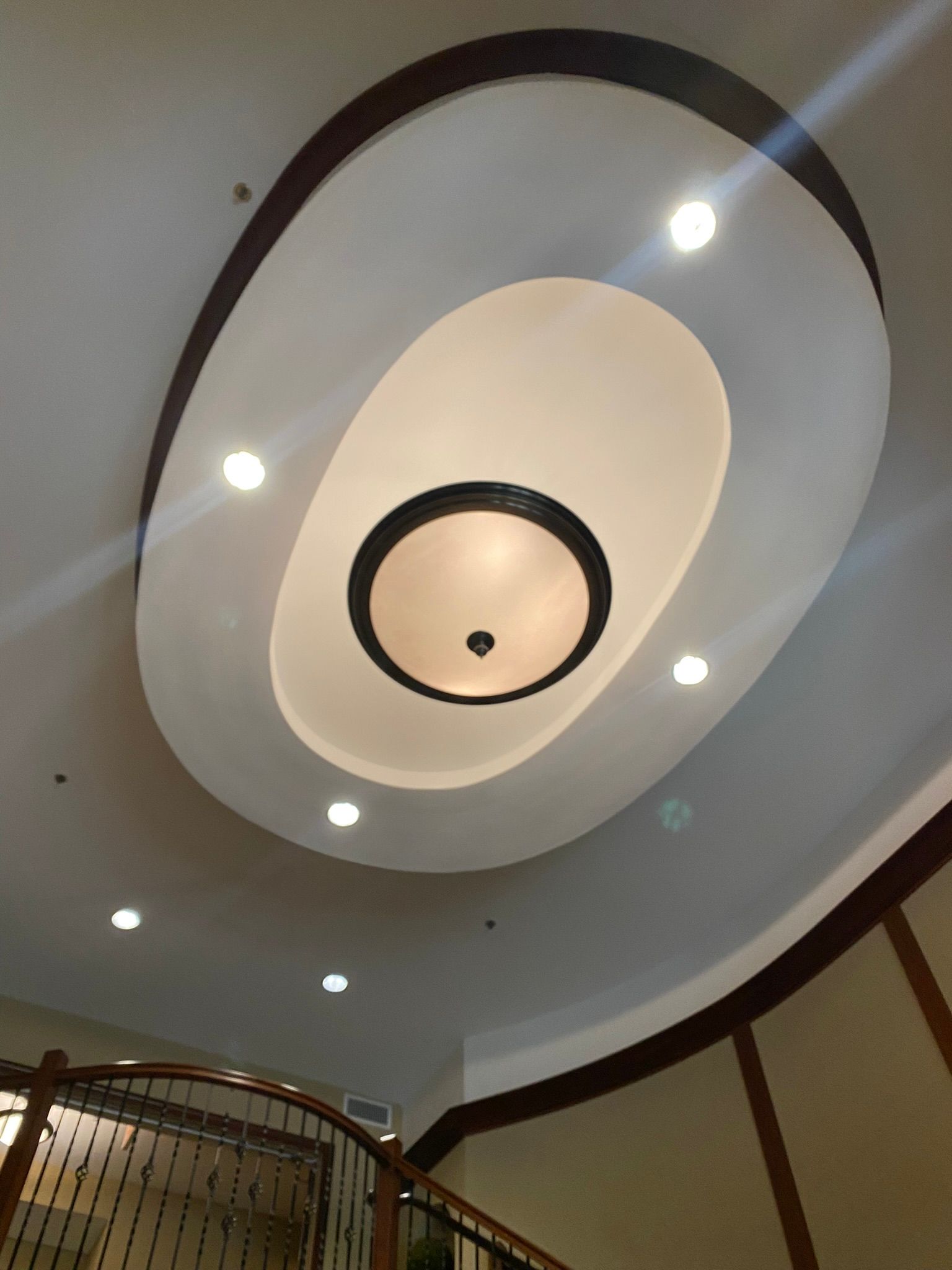 Oval recessed ceiling with layered lighting and dark wood trim above a staircase.