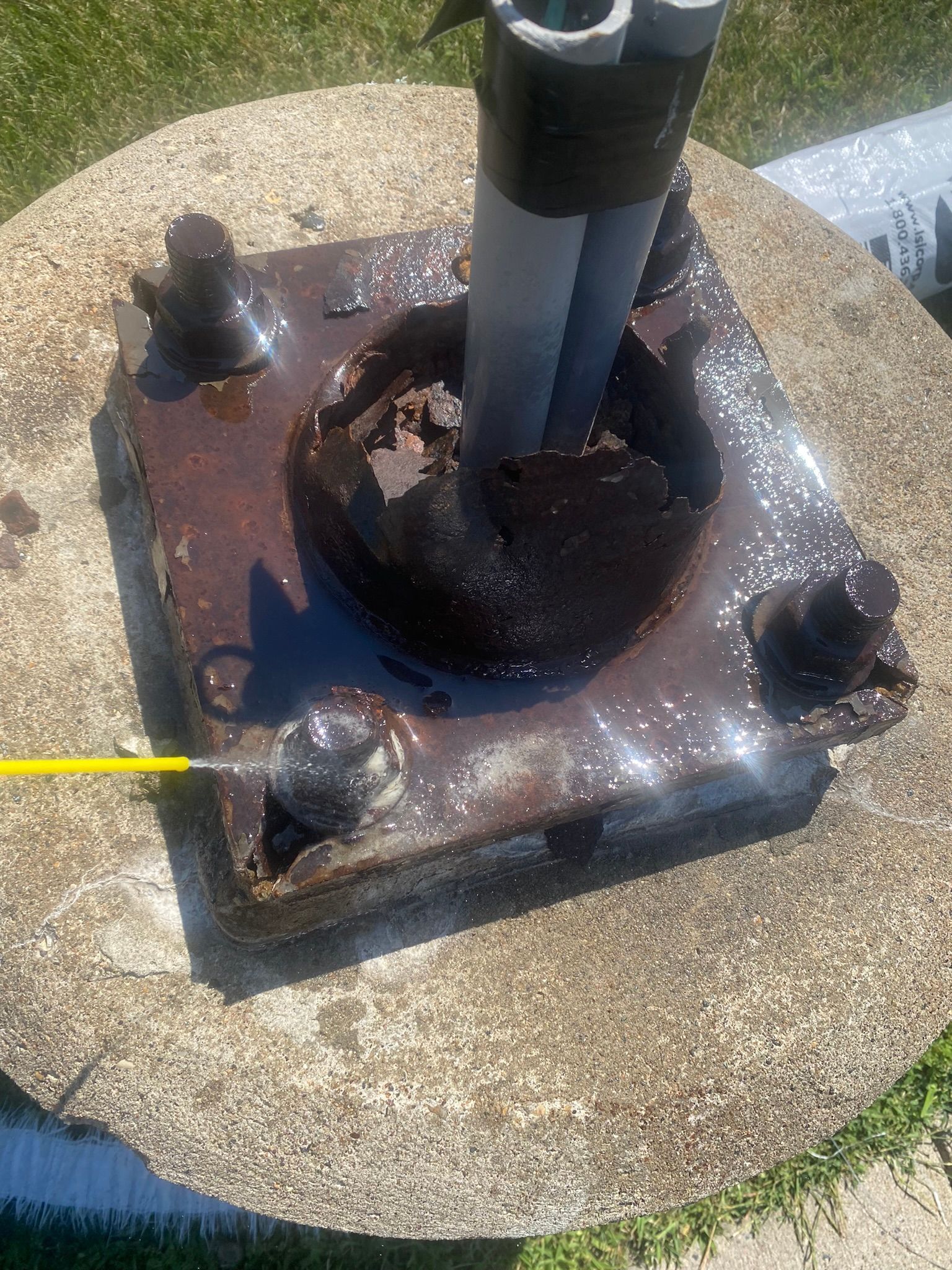 Rusty metal base of a pole bolted to a concrete slab, with water and a yellow object.