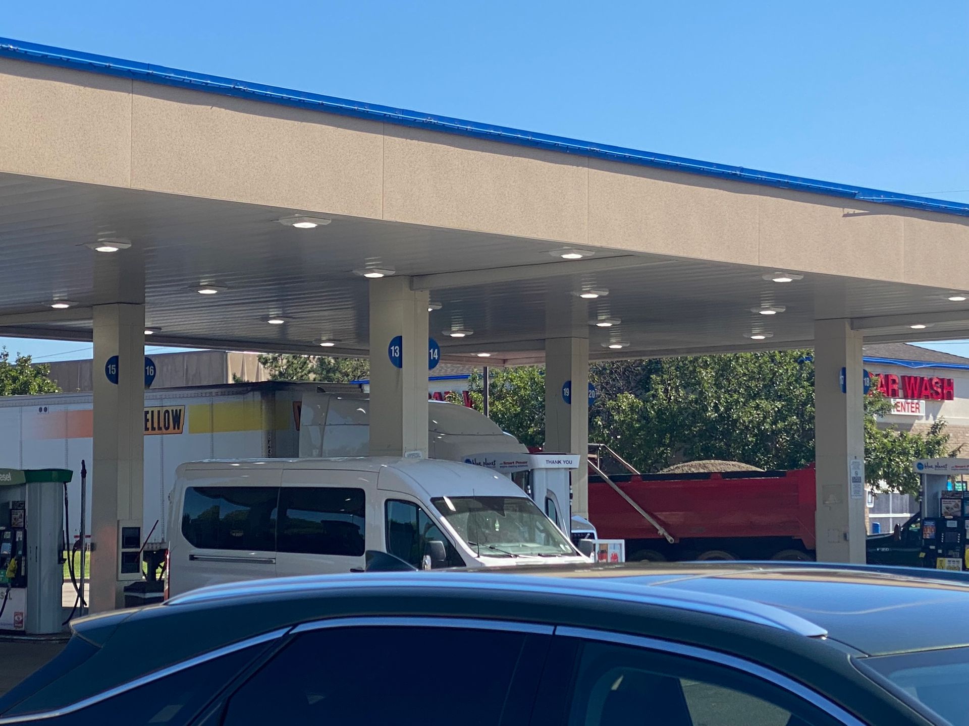 A white van parked at a gas station under a canopy with several cars.