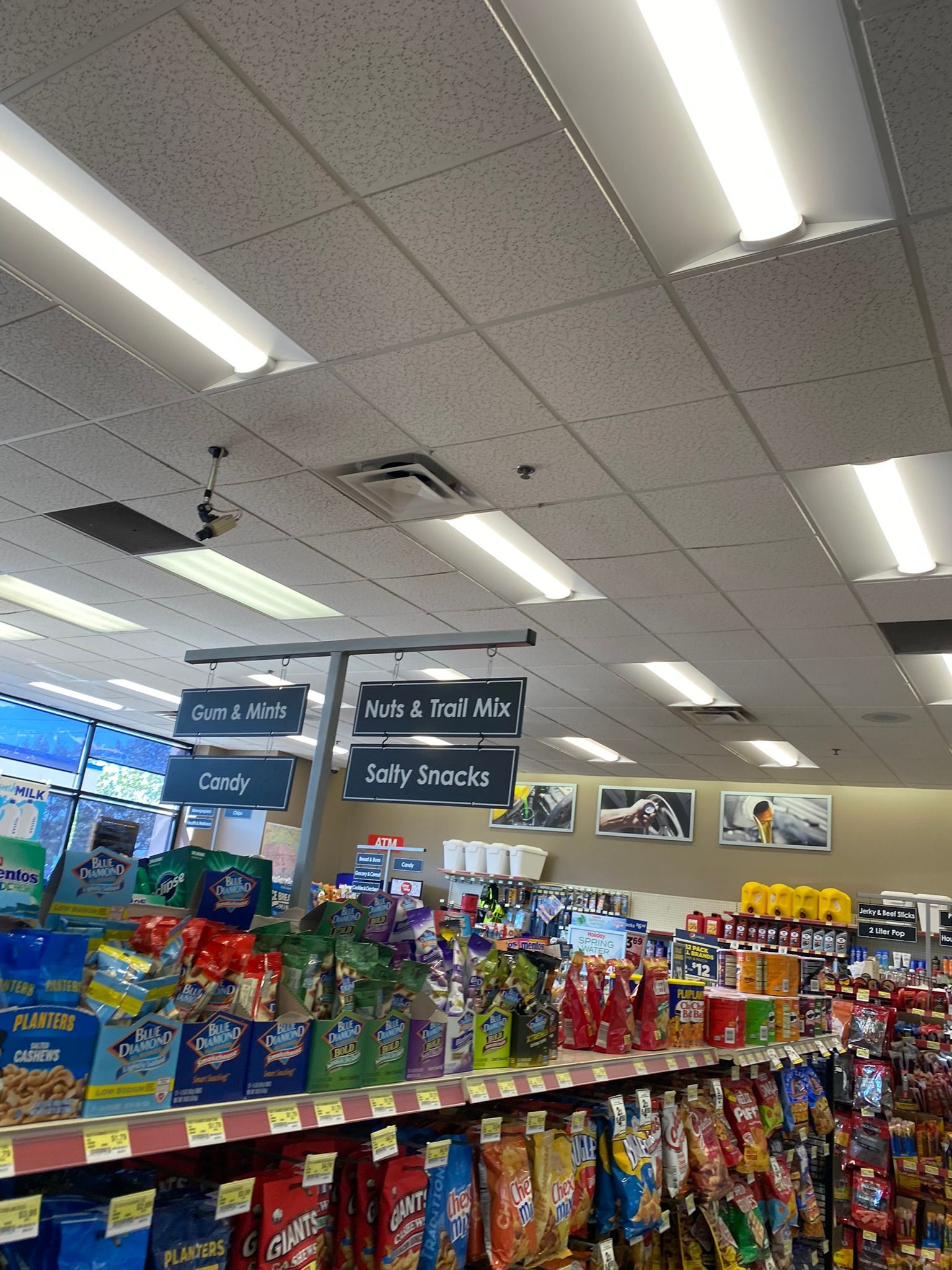 Grocery store aisle with overhead signs, snacks on shelves, and bright fluorescent lights.