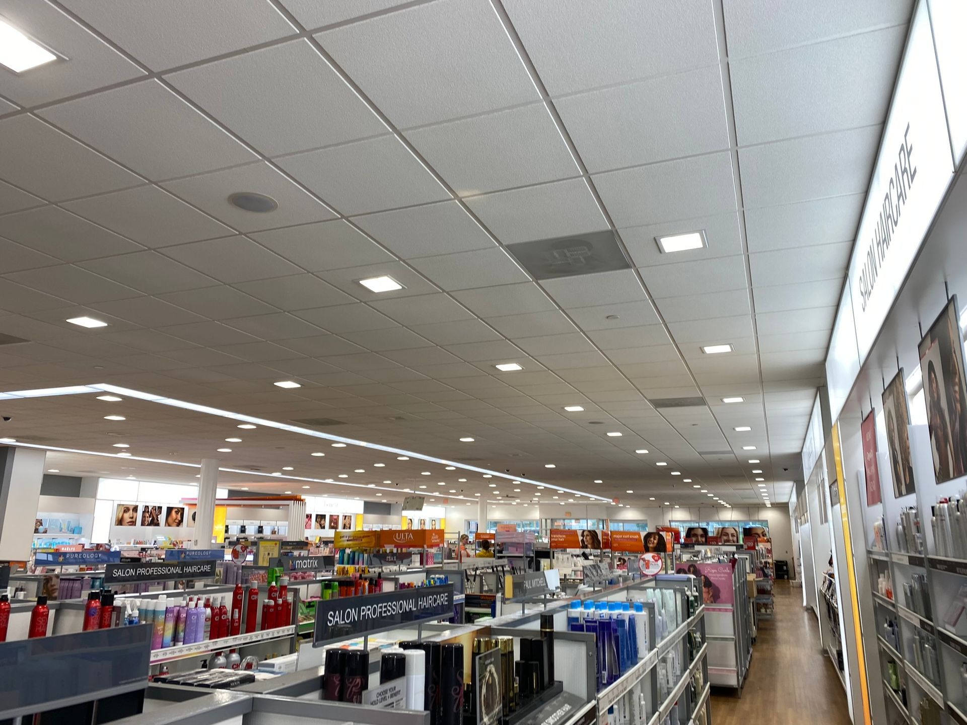 Inside a brightly lit store with shelves and displays of products, view down an aisle.