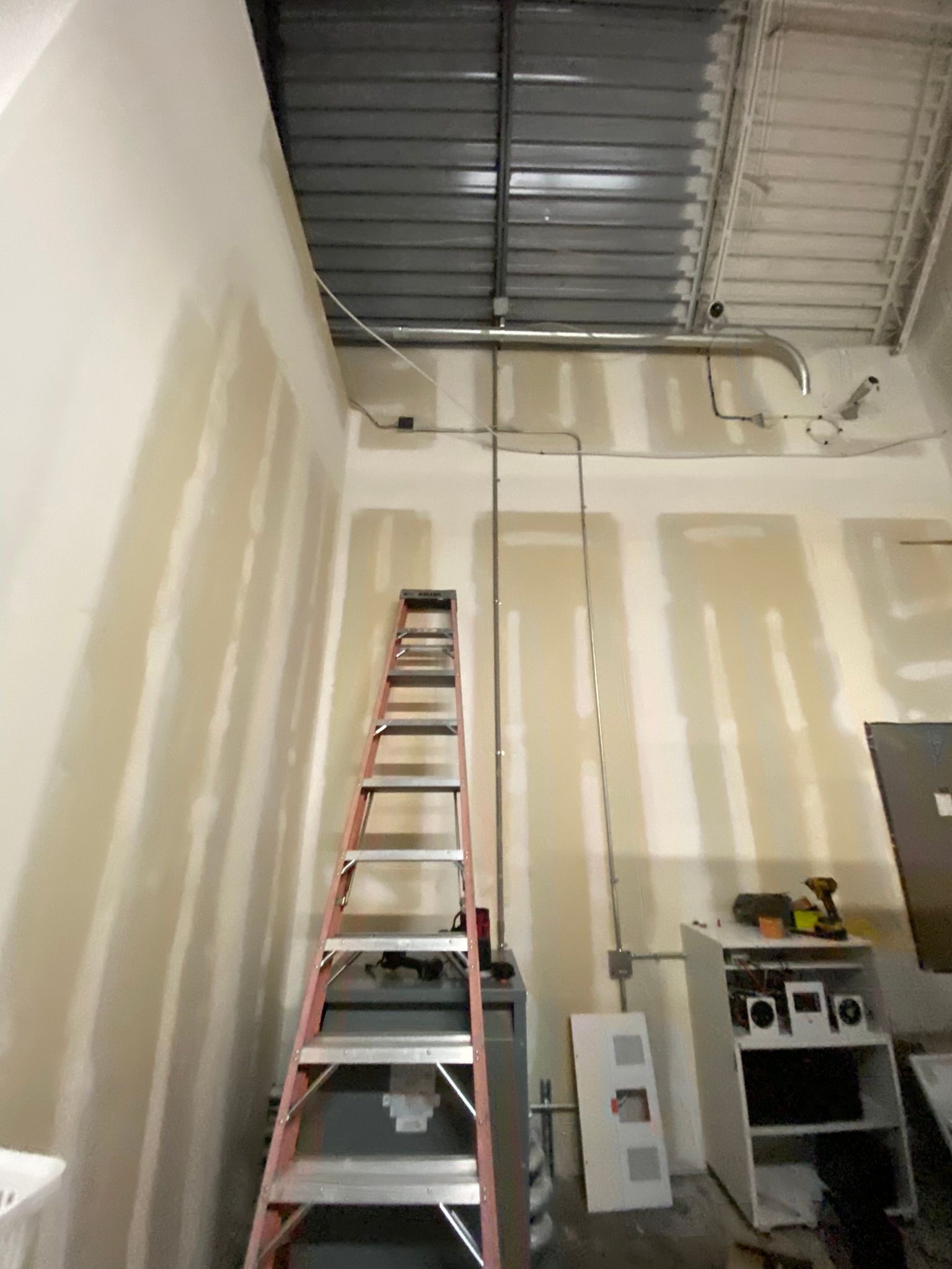 A ladder stands against a wall with exposed wiring and ceiling, likely under construction.
