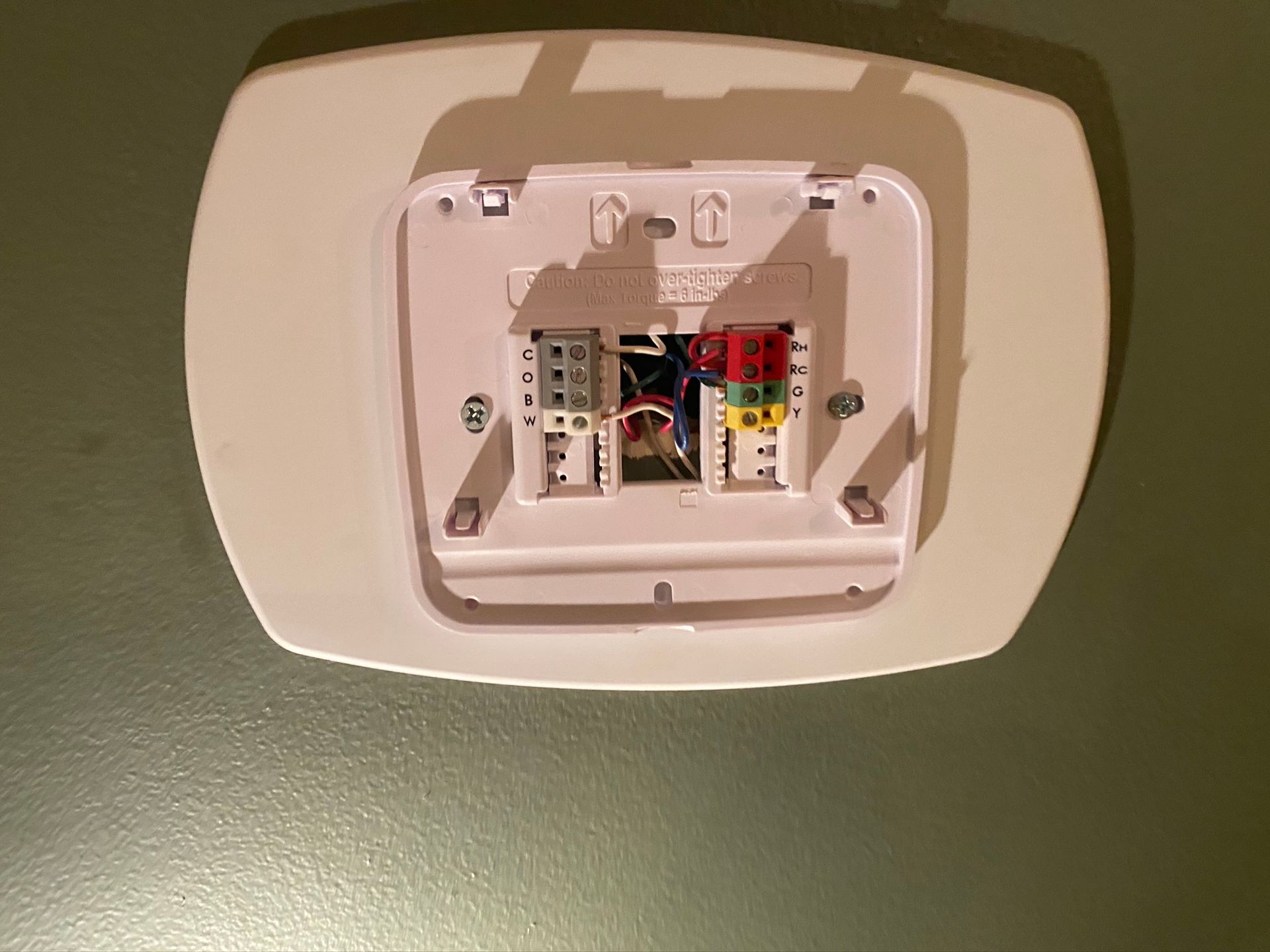 Thermostat base with colored wires connected, mounted on a green wall.