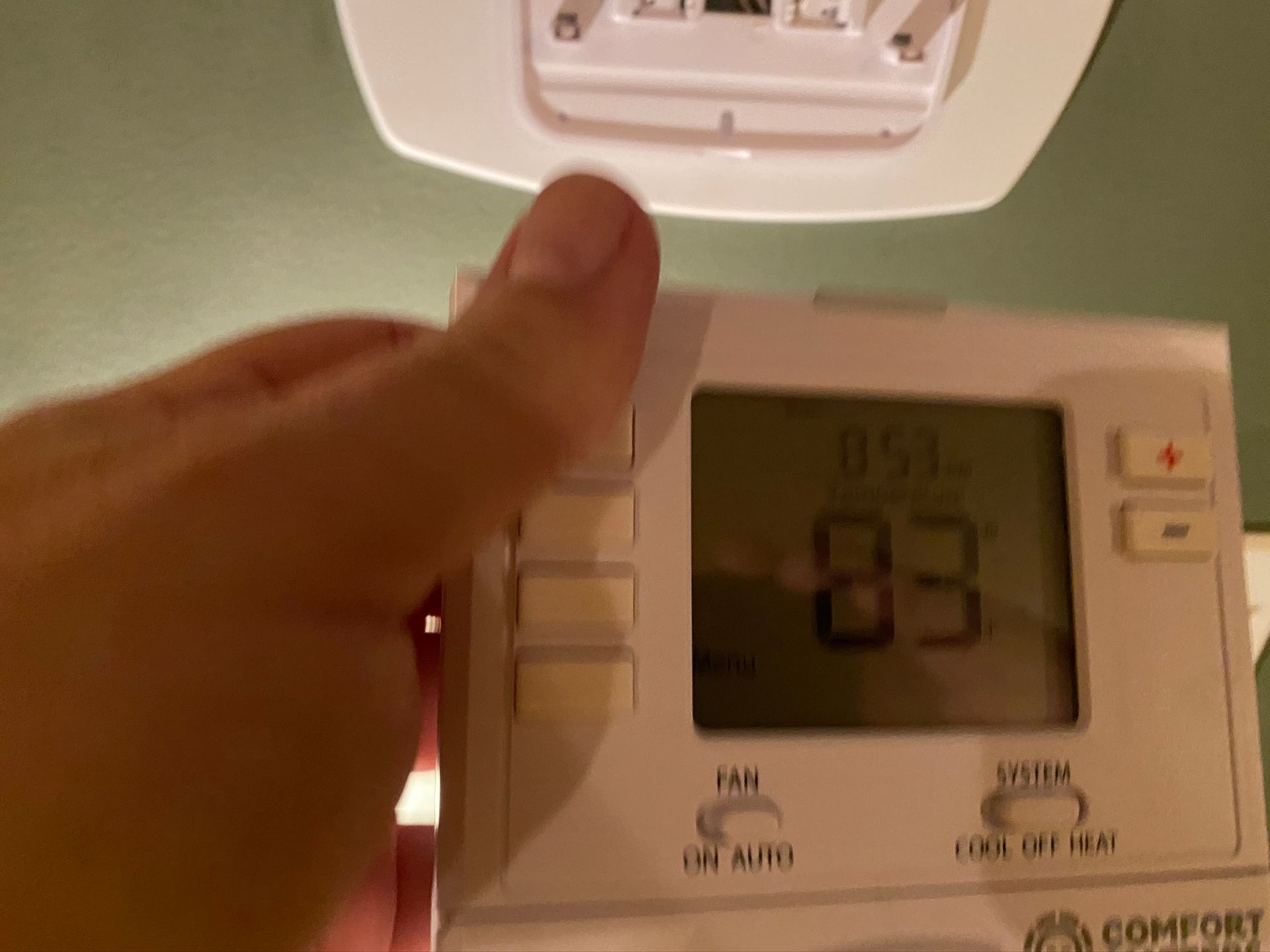Hand adjusting a thermostat; display reads 83 degrees.