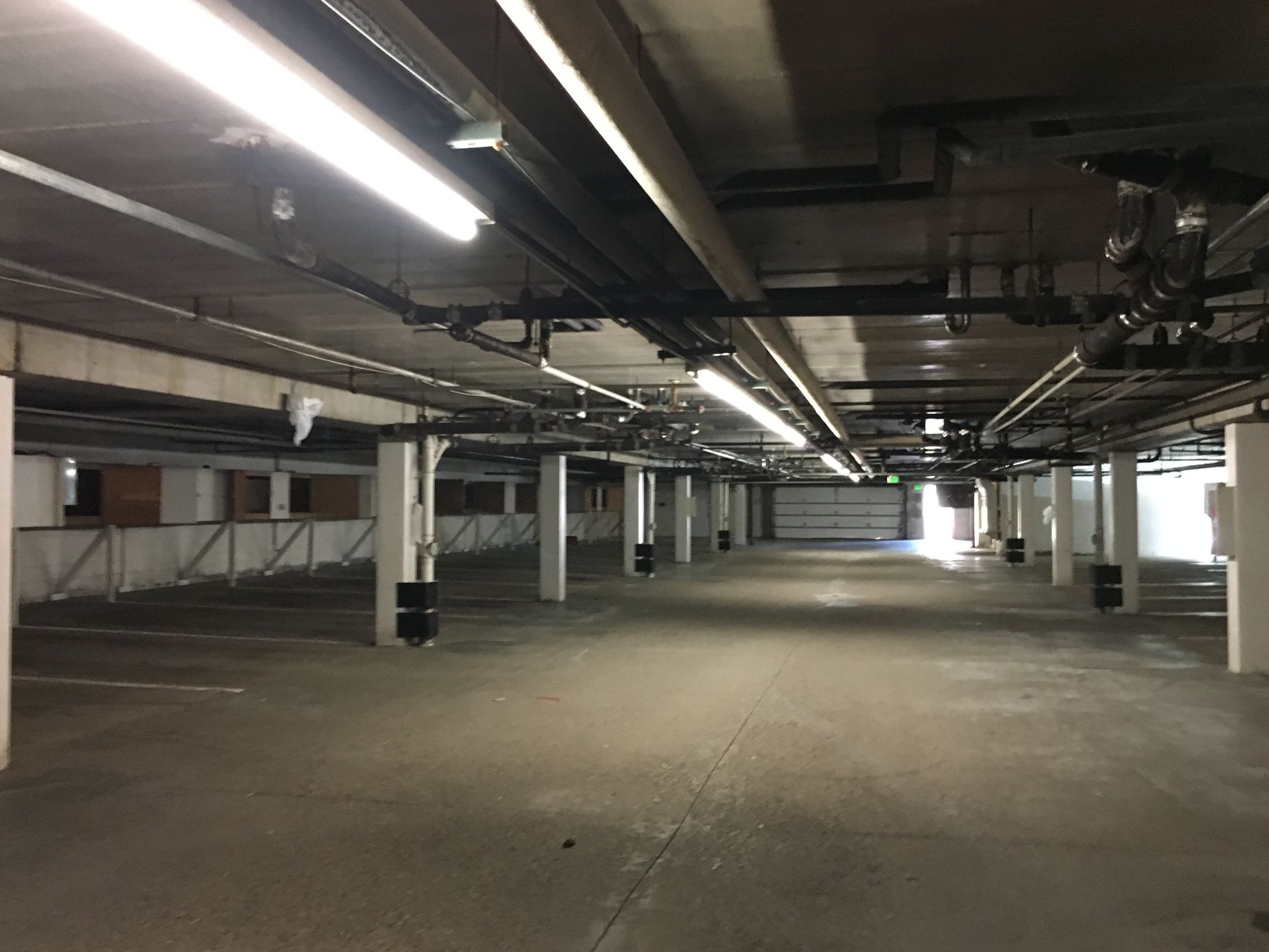 Empty underground parking garage with concrete floor, pillars, and overhead pipes.