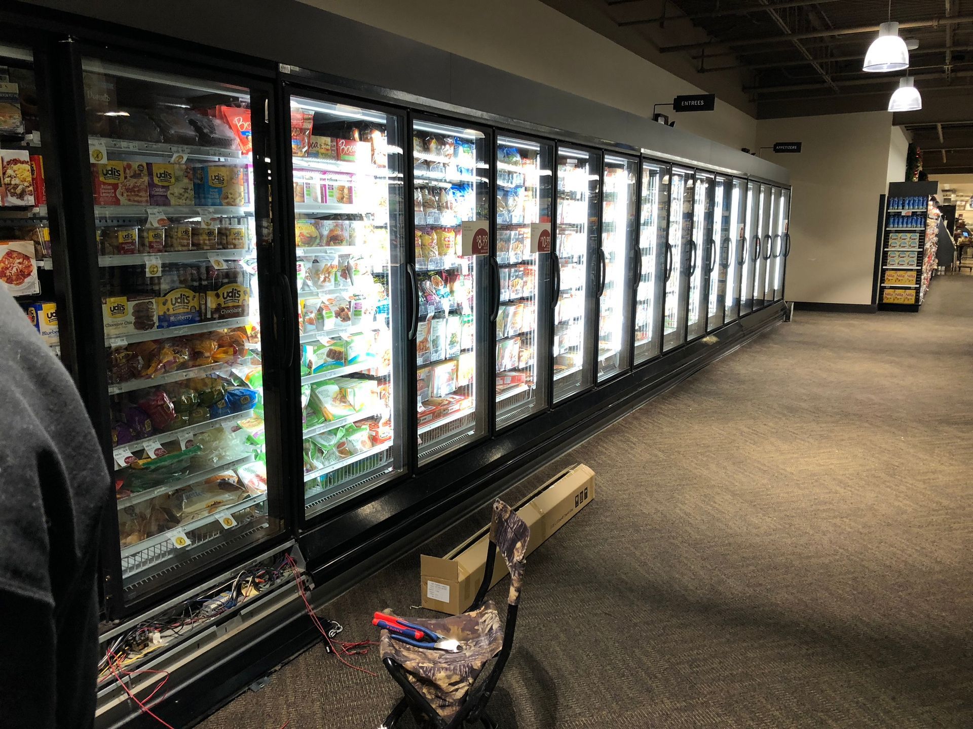 A long row of lit refrigerator cases in a grocery store aisle, displaying various food items.