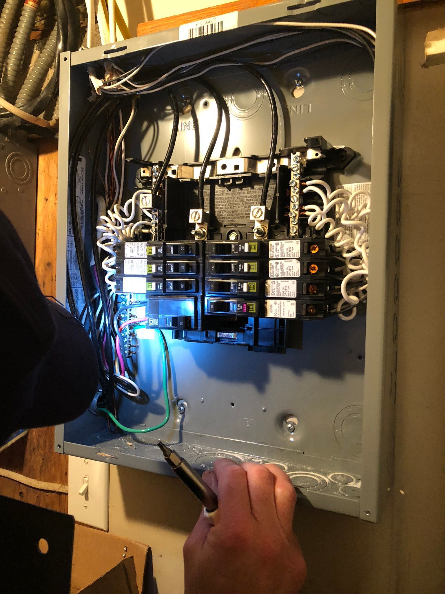 Person working on an electrical panel, testing a wire. The panel is gray, the wires are various colors.