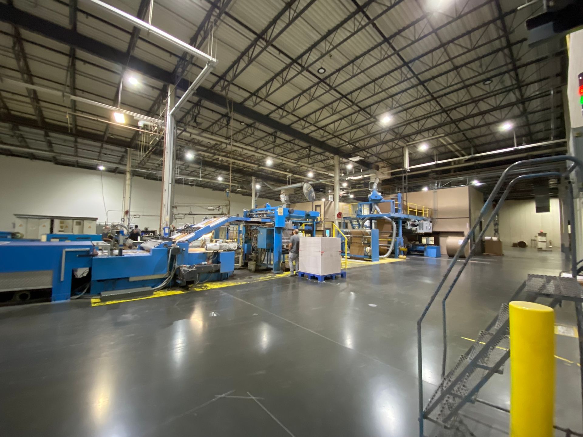 Factory interior with blue machinery and a gray floor; overhead lighting.