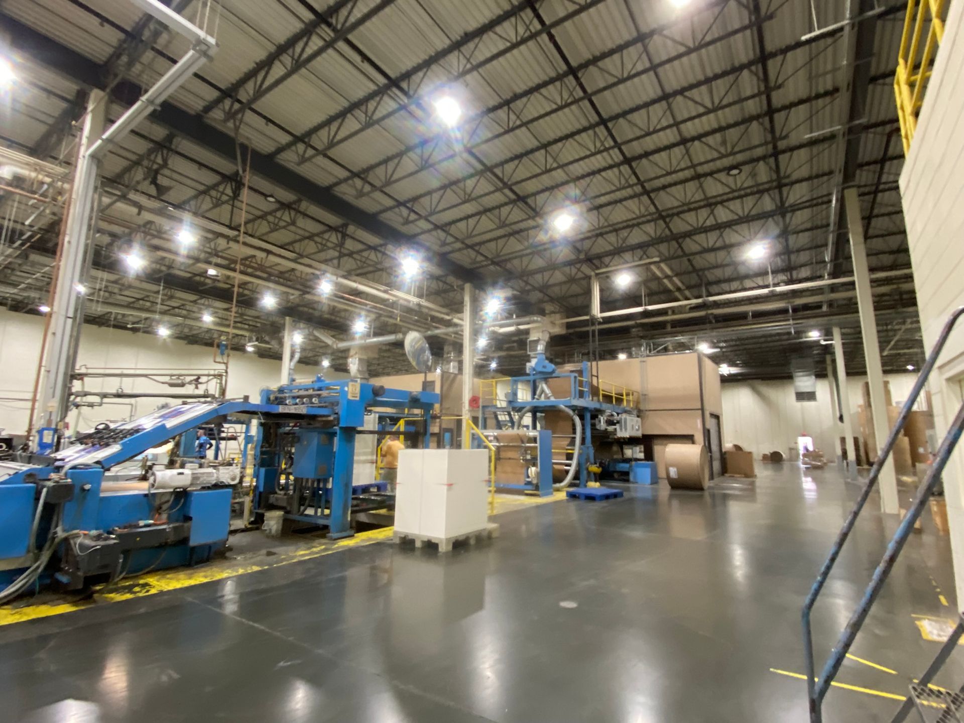 Industrial interior with blue machinery and cardboard boxes on a gray floor.