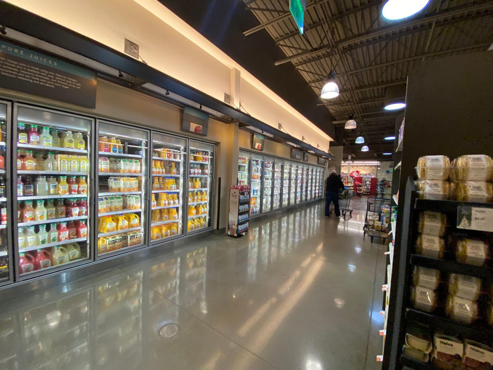 Refrigerated beverage aisle in a brightly lit grocery store. A person walks toward the back.