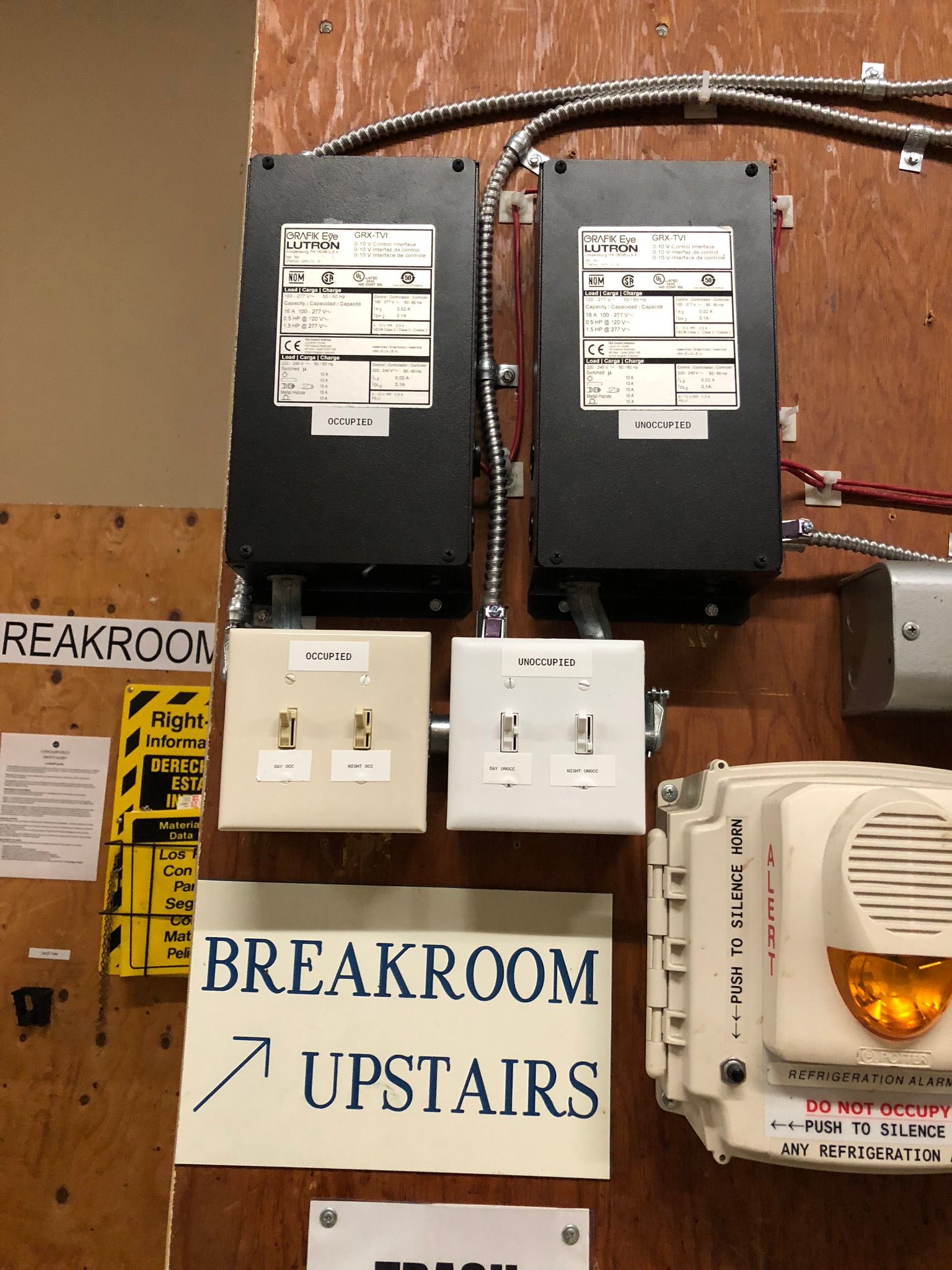 Electrical boxes and outlets mounted on a wooden wall, with a breakroom sign pointing upward.