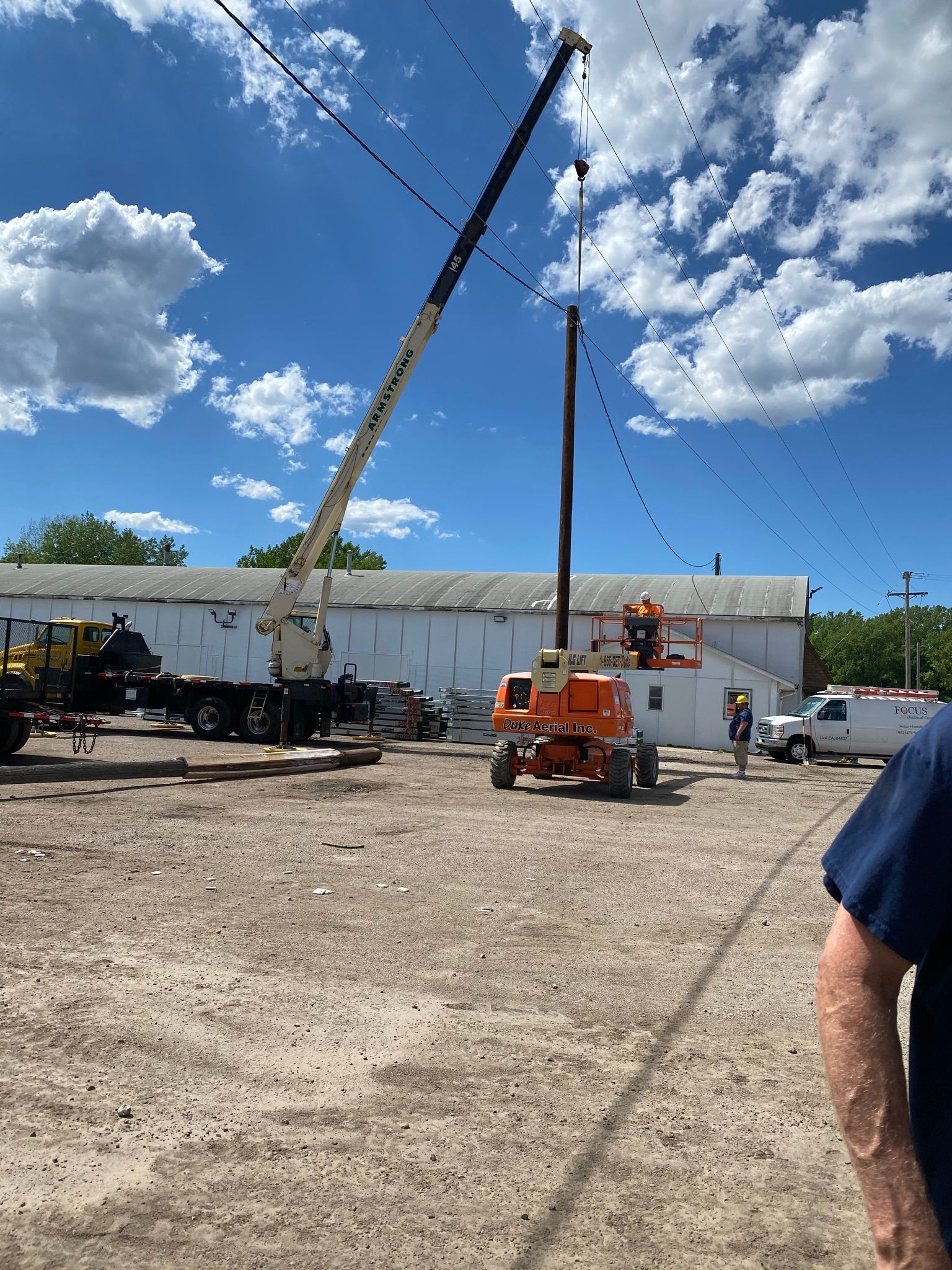 Cranes and lift platform at a construction site with workers. Blue sky and clouds in the background.