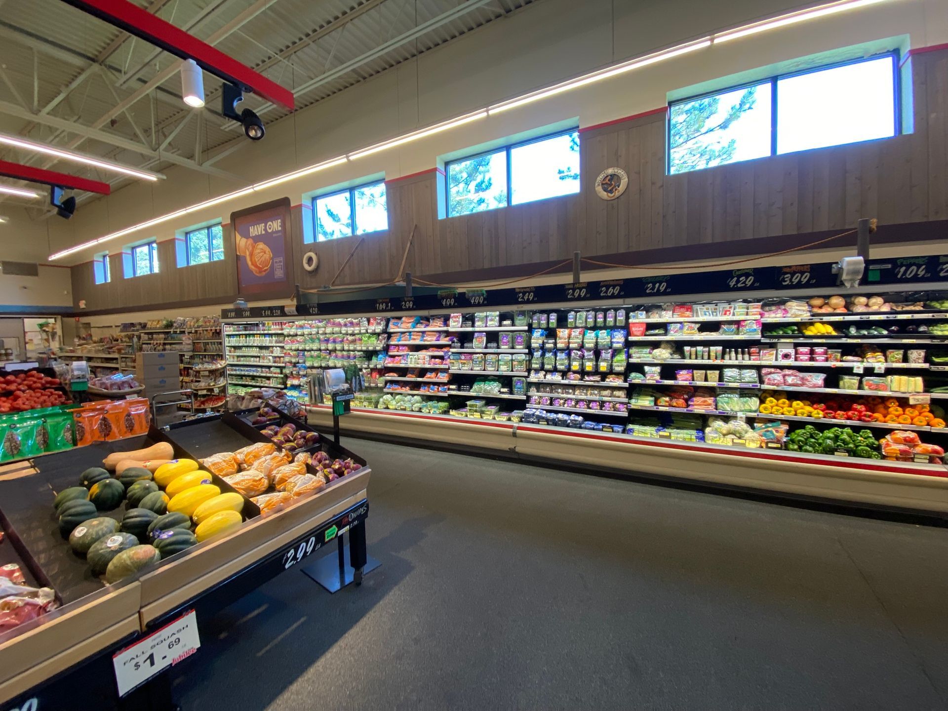 Produce aisle in a grocery store, displaying various fruits and vegetables under bright lights.