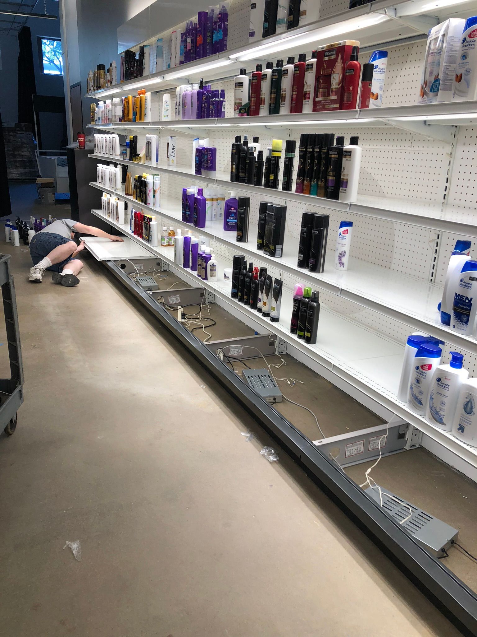 Person installing shelf in a store aisle with shampoo and conditioner on shelves.