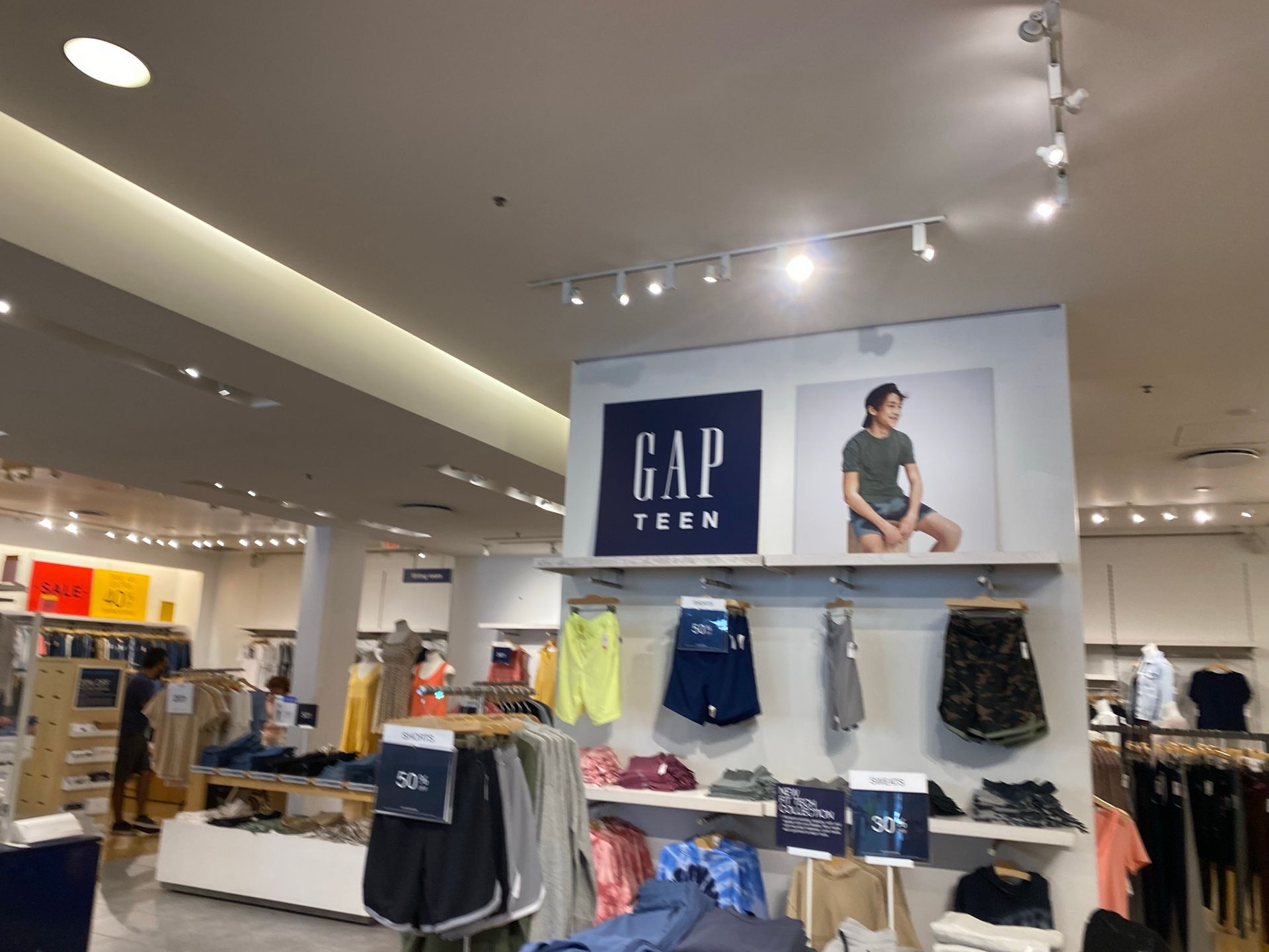 Gap Teen clothing display in a retail store with apparel on shelves and racks under the store's logo.