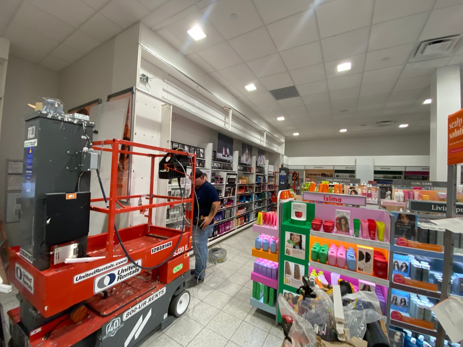 A person works near shelves of products in a store, using a lift.