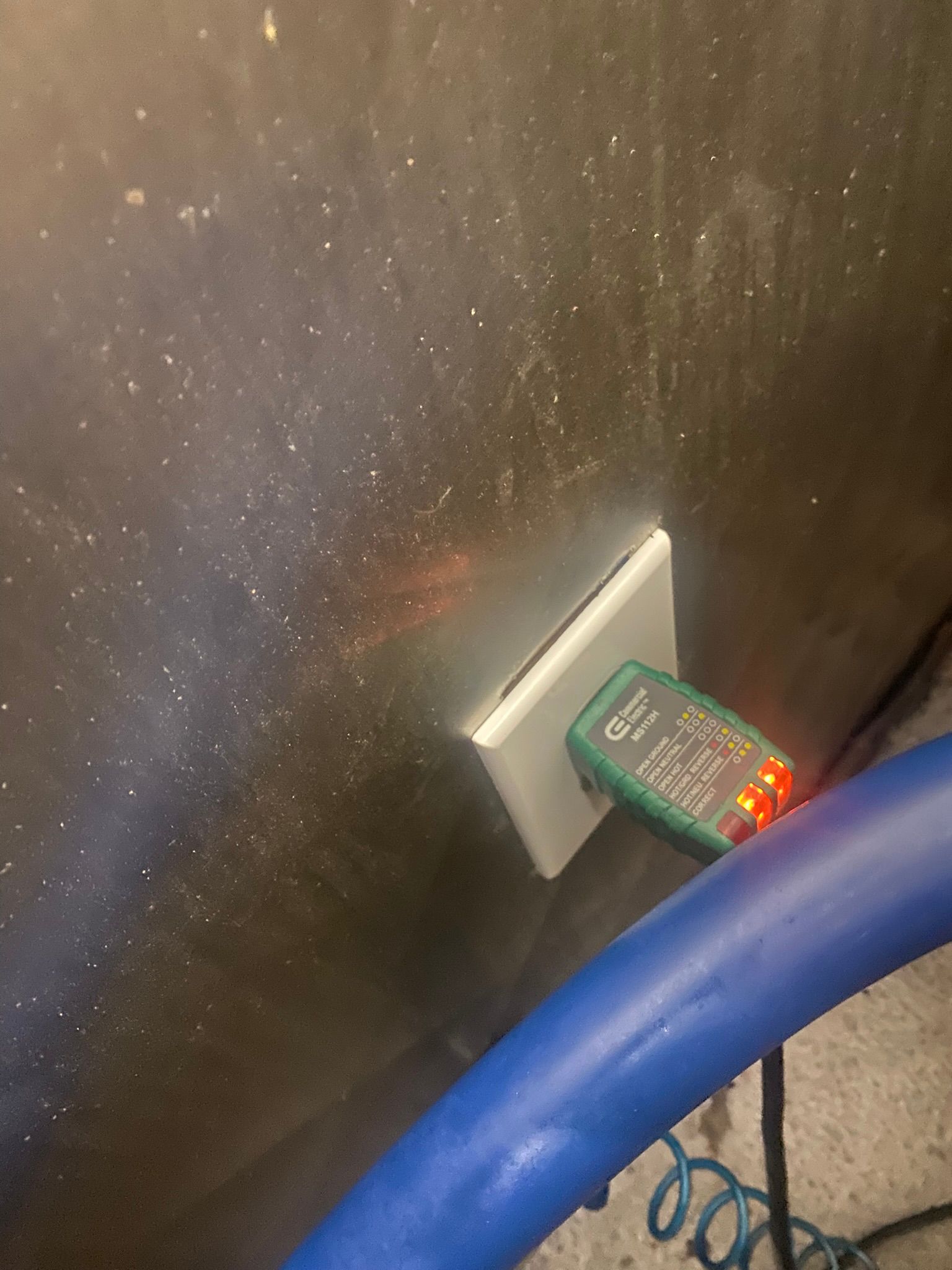 Outlet with electrical tester lit up, indicating a wiring issue. Blue hose visible.