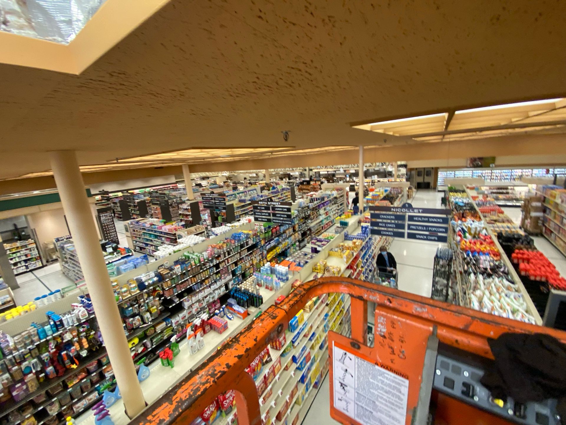 Overhead view of a grocery store from a lift. Rows of shelves filled with products, a person operates the lift.
