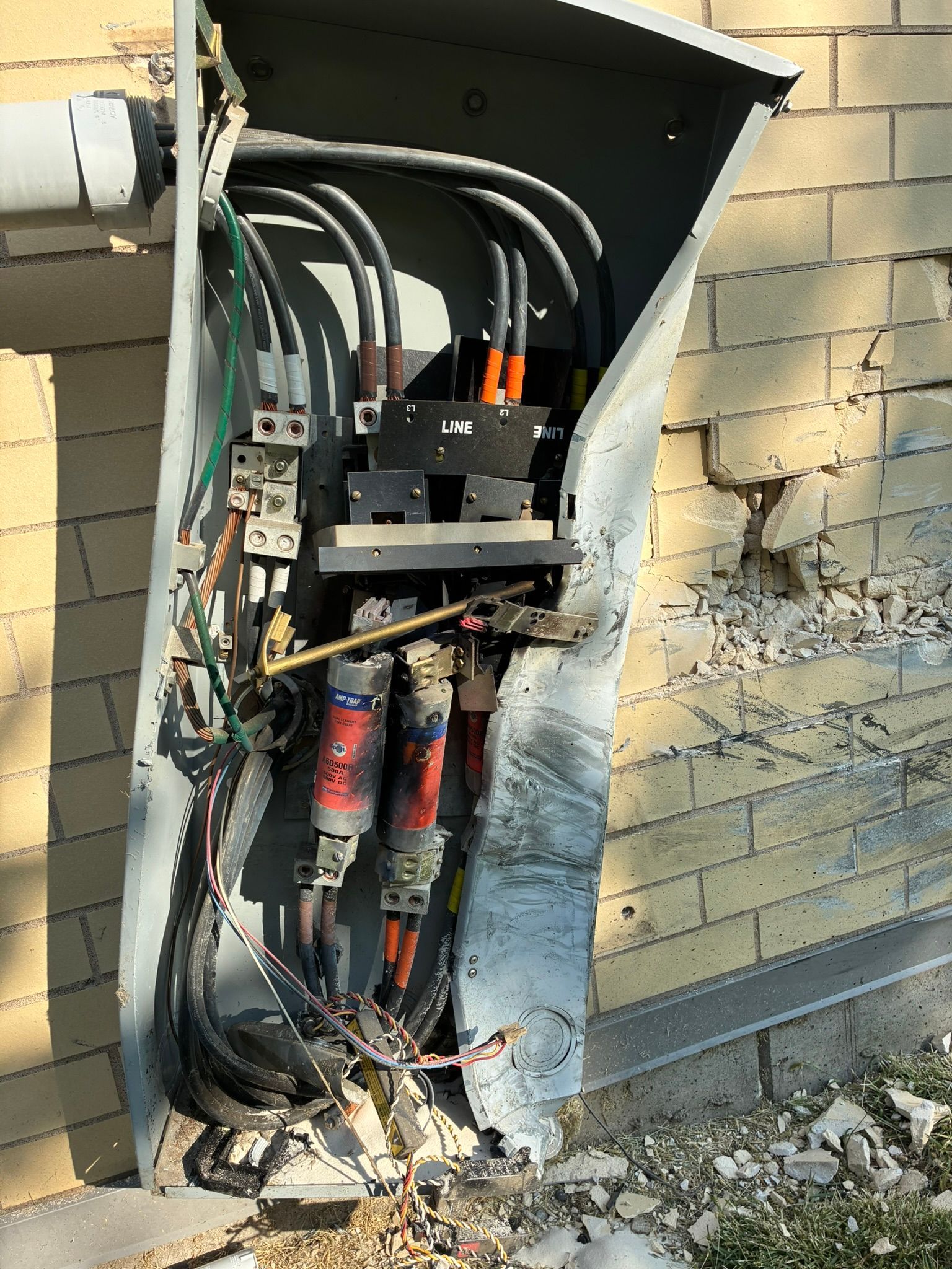 Damaged electrical box on a brick wall, wires exposed and damaged.