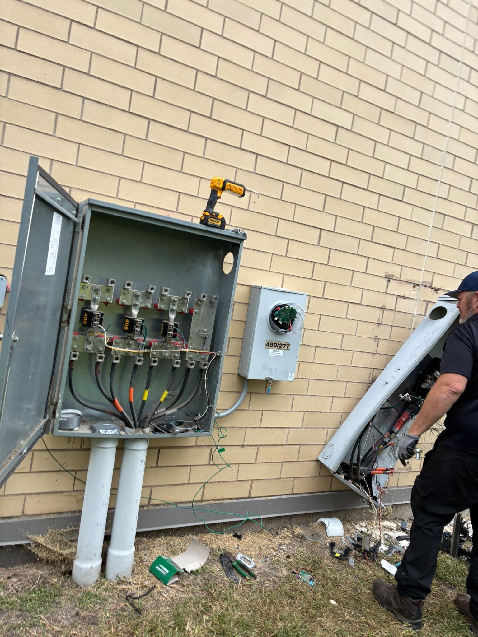Electrician removing a metal electrical box from a building. Wires exposed. Yellow siding.