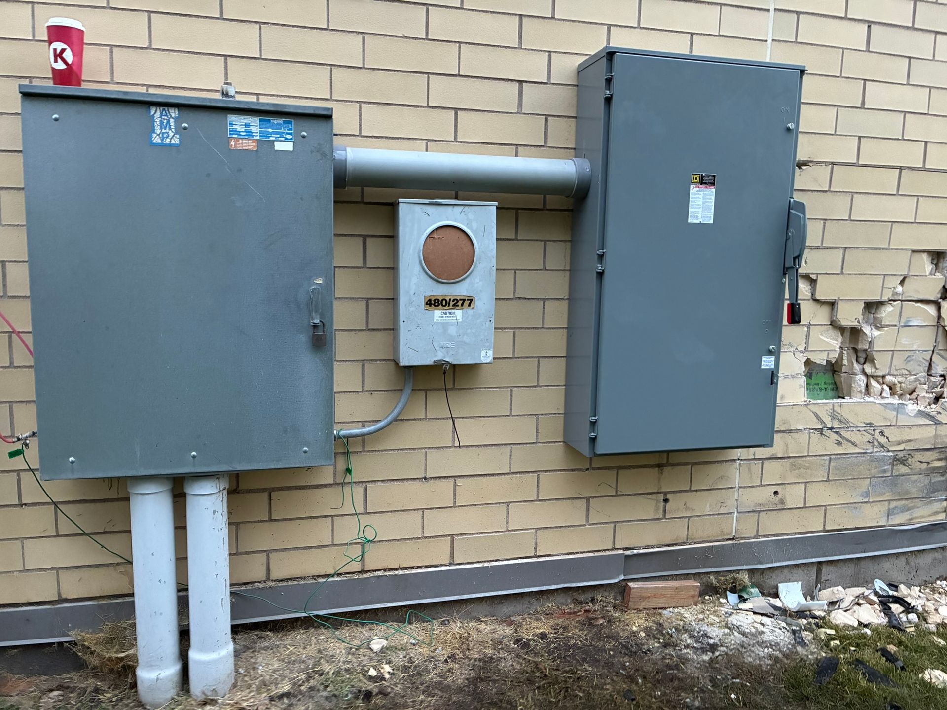Electrical boxes attached to a brick wall. Gray boxes with conduit and meter.